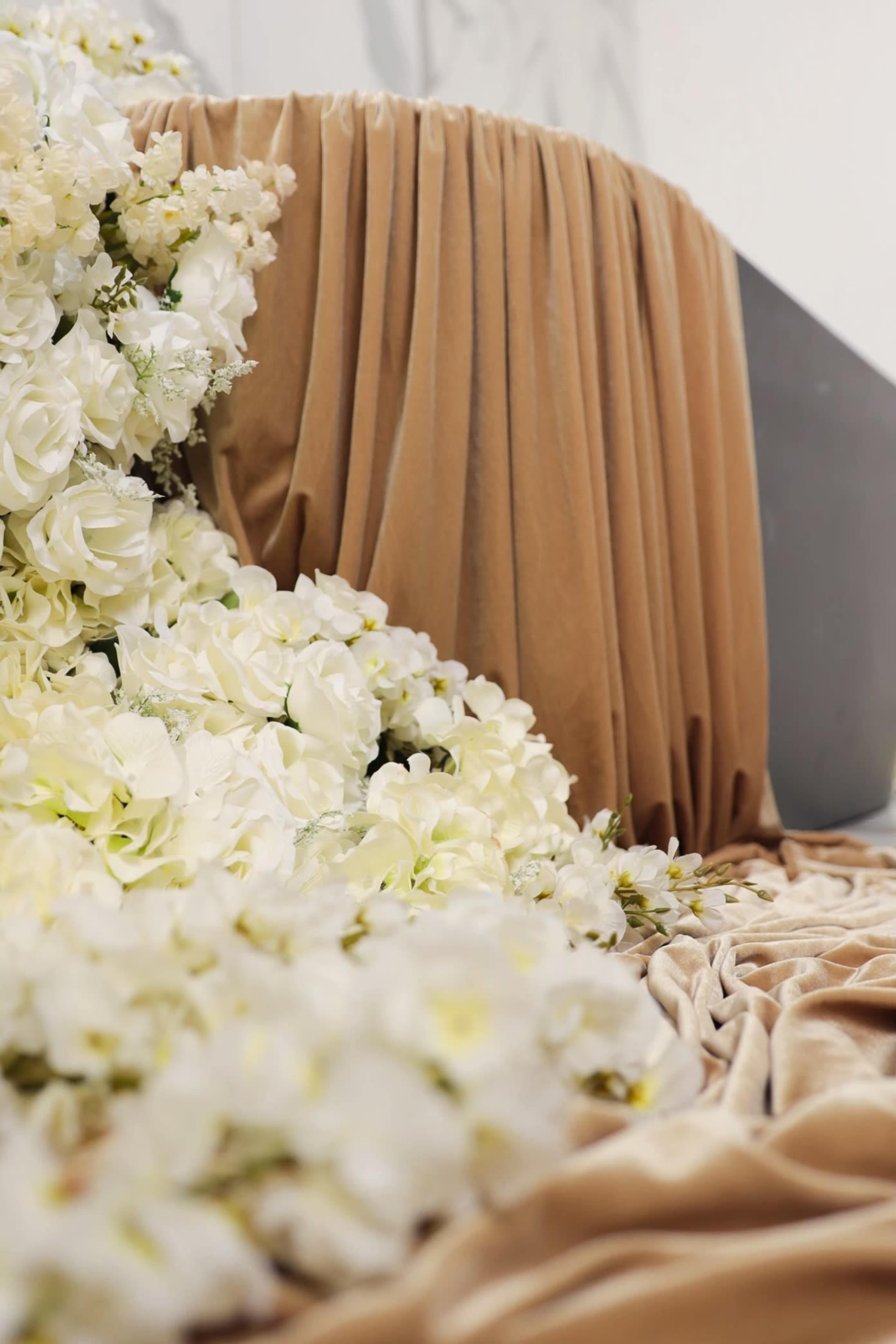 A cascade of white flowers rests against a draped beige fabric backdrop.