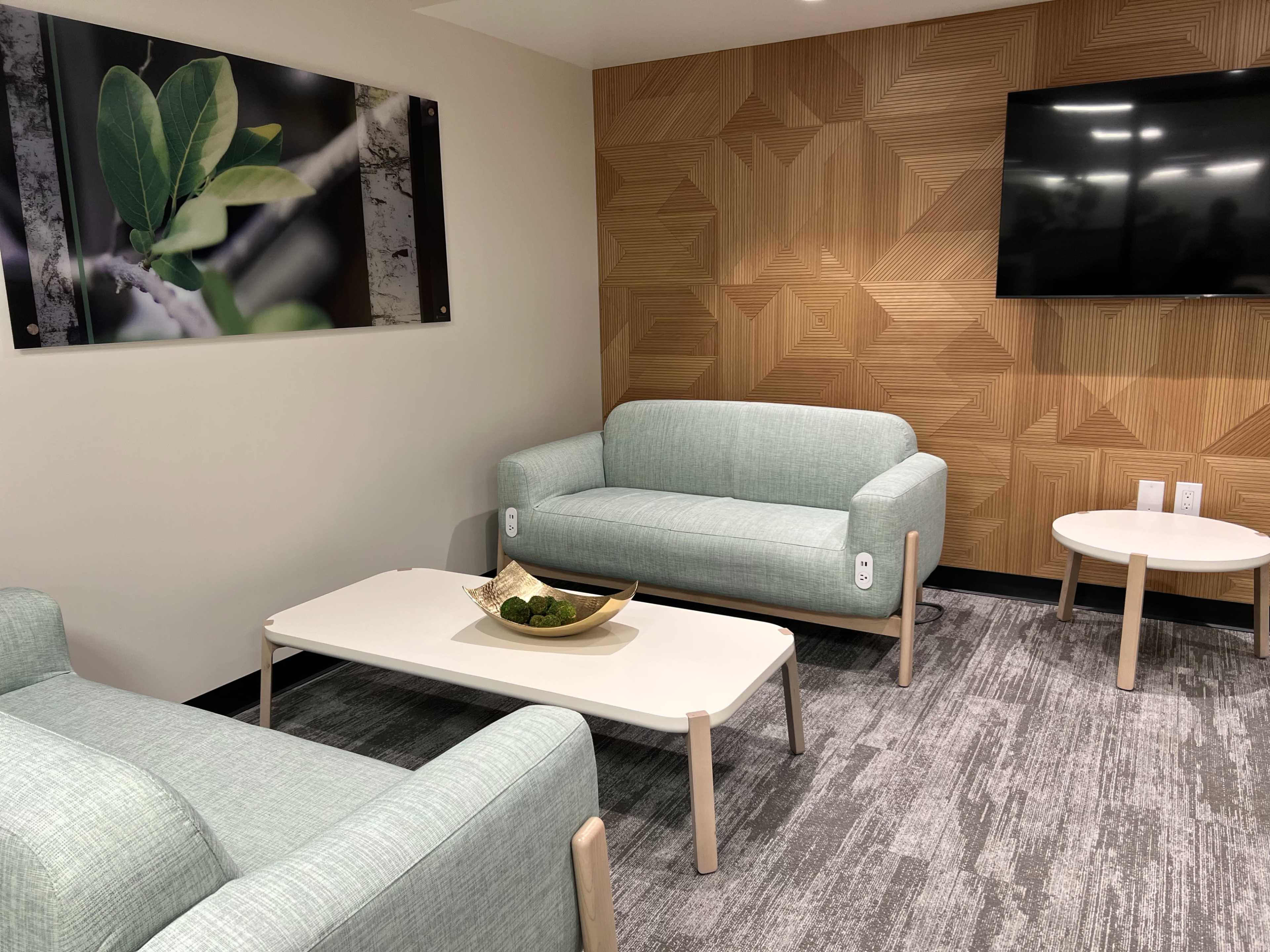 A modern lounge area with two light blue sofas, a white coffee table, a small side table, and a wooden wall featuring a geometric design.
