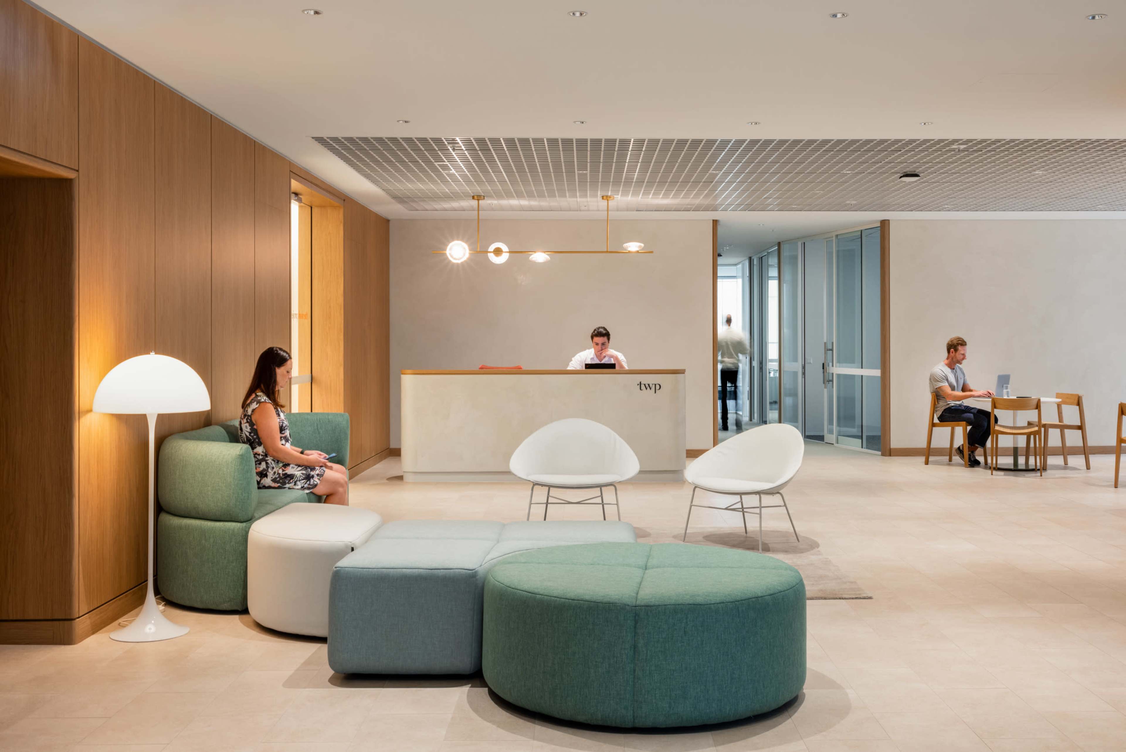 The image shows a modern reception area with a seating arrangement, a reception desk, and a few people working or waiting.