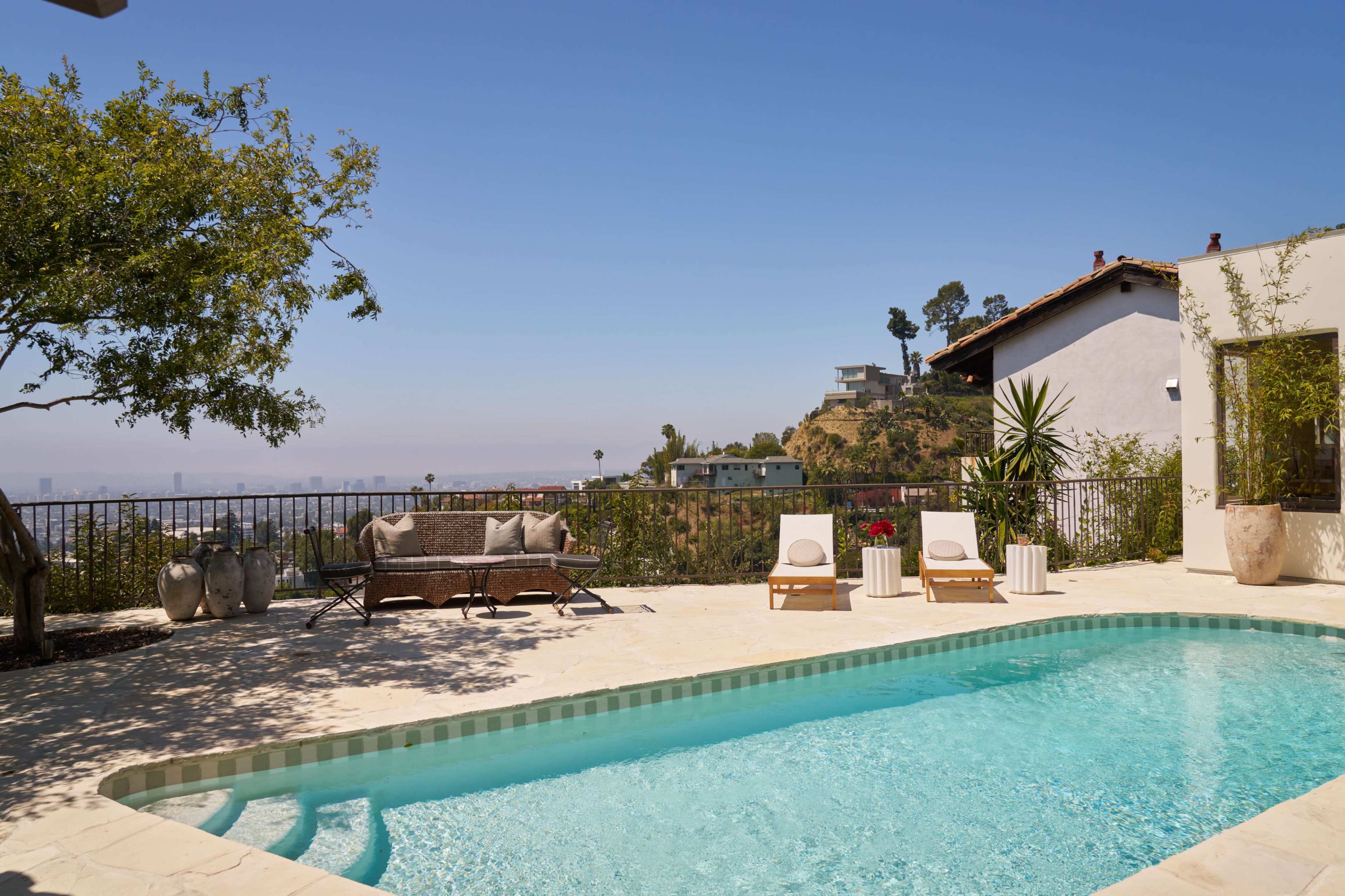 The image shows a backyard area with a swimming pool, two lounge chairs, and a view of hills and houses under a clear blue sky.
