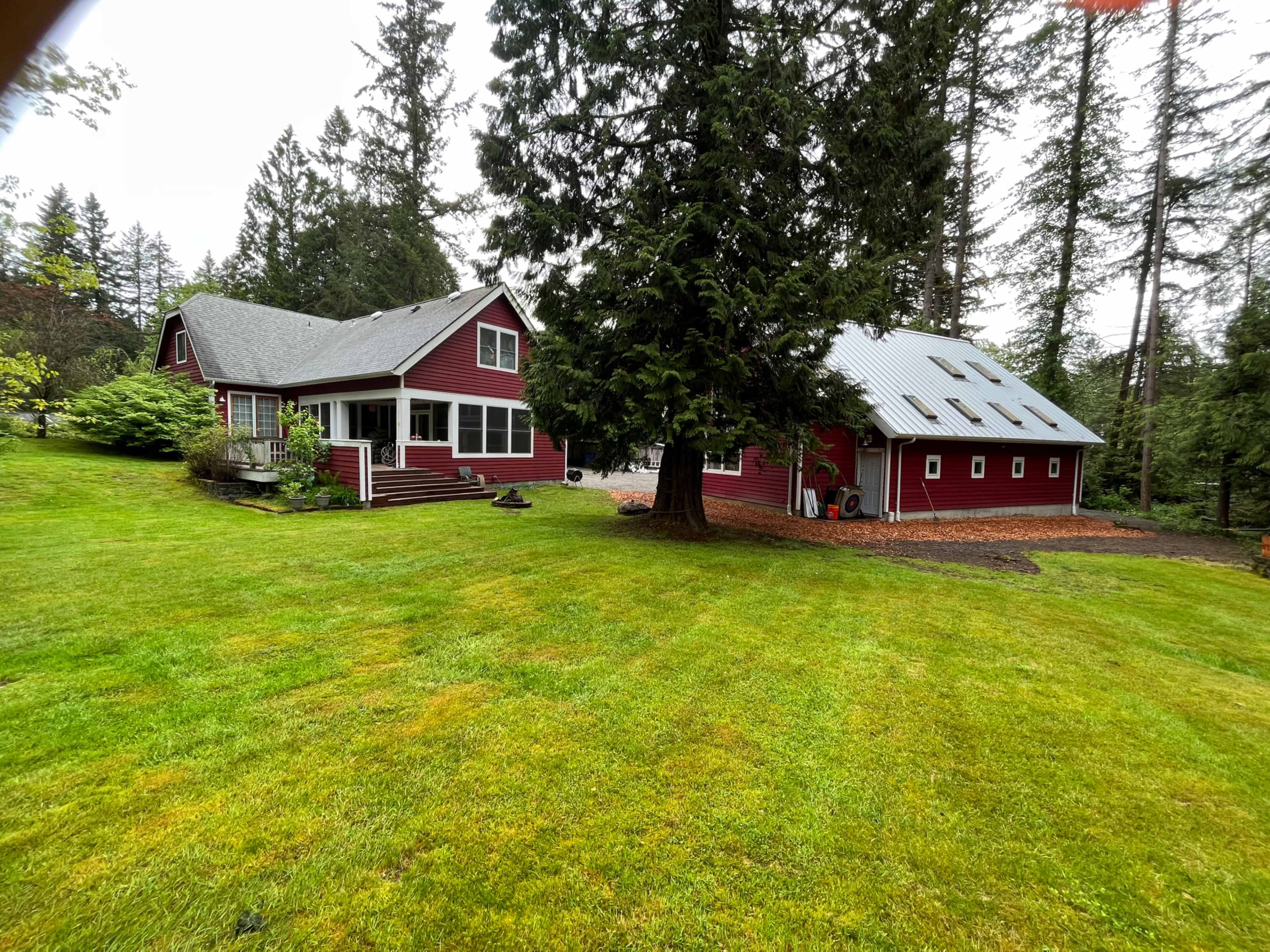 The image shows a red farmhouse with a gray roof, surrounded by a grassy lawn and tall trees.