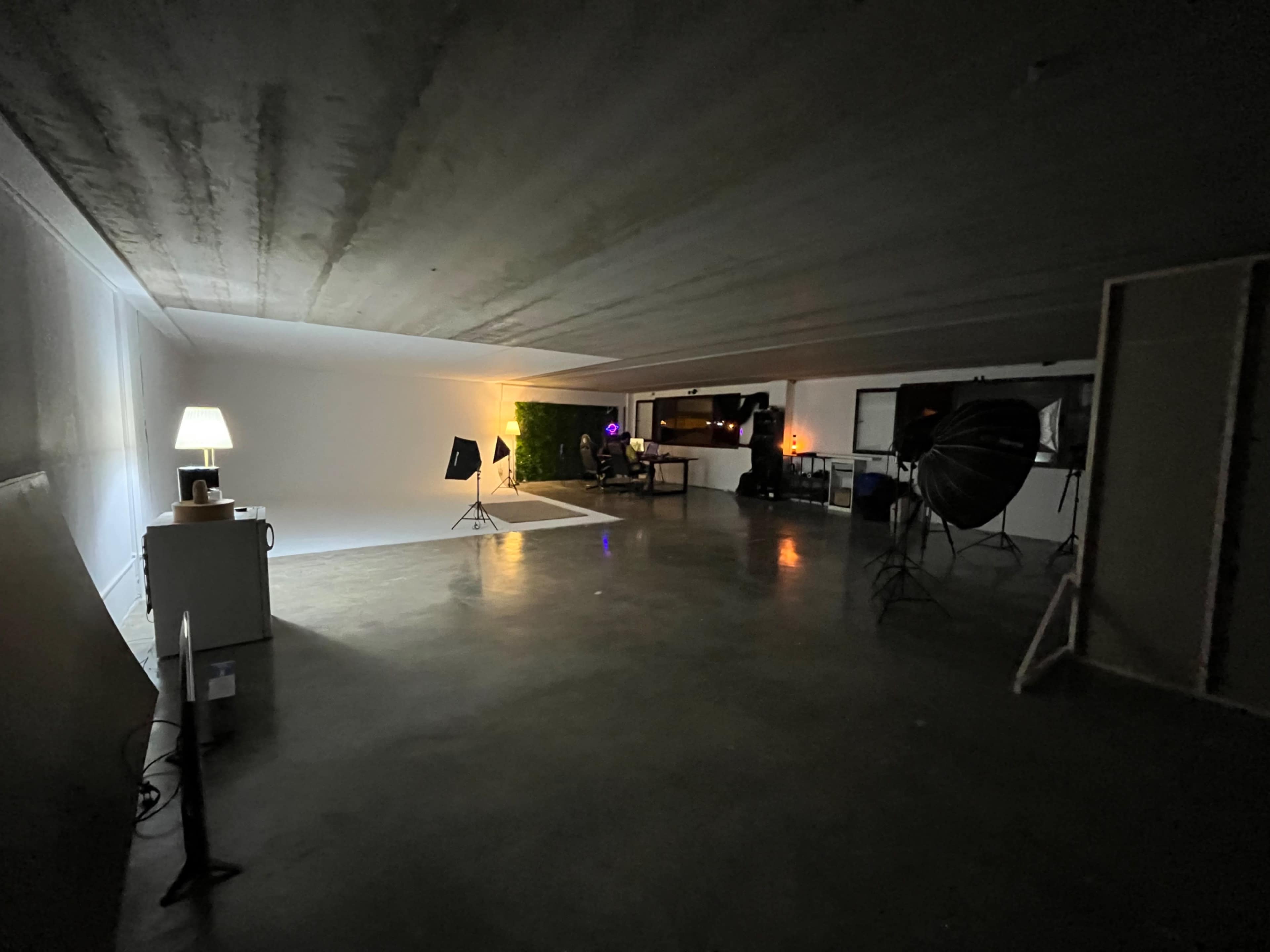A spacious photography studio with a white backdrop, lighting equipment, and a large window reflecting a dimly lit area.