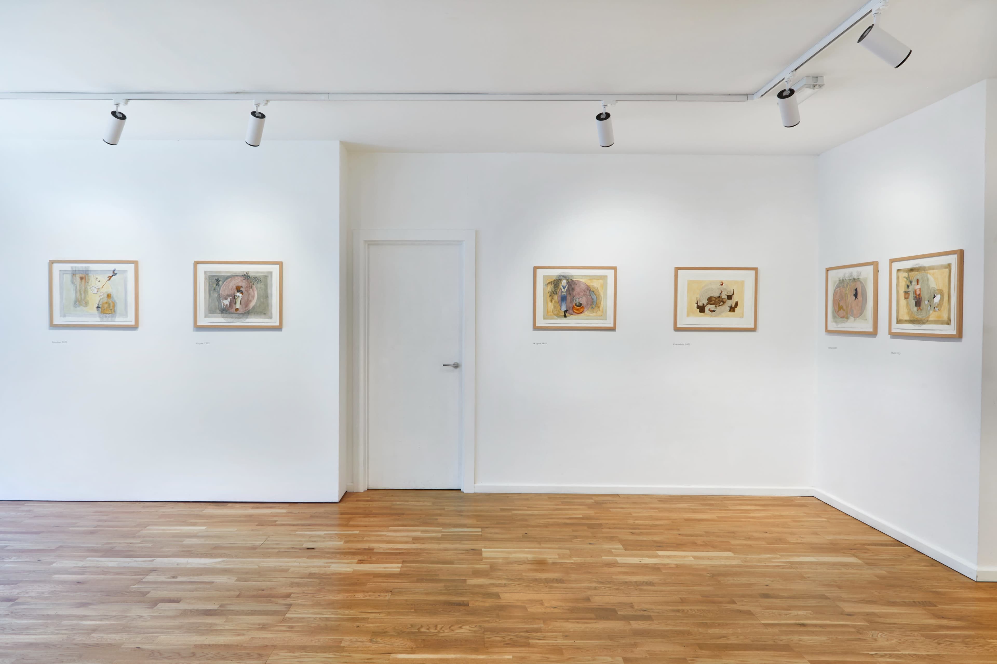 An art gallery with framed artworks displayed on white walls and wooden flooring.