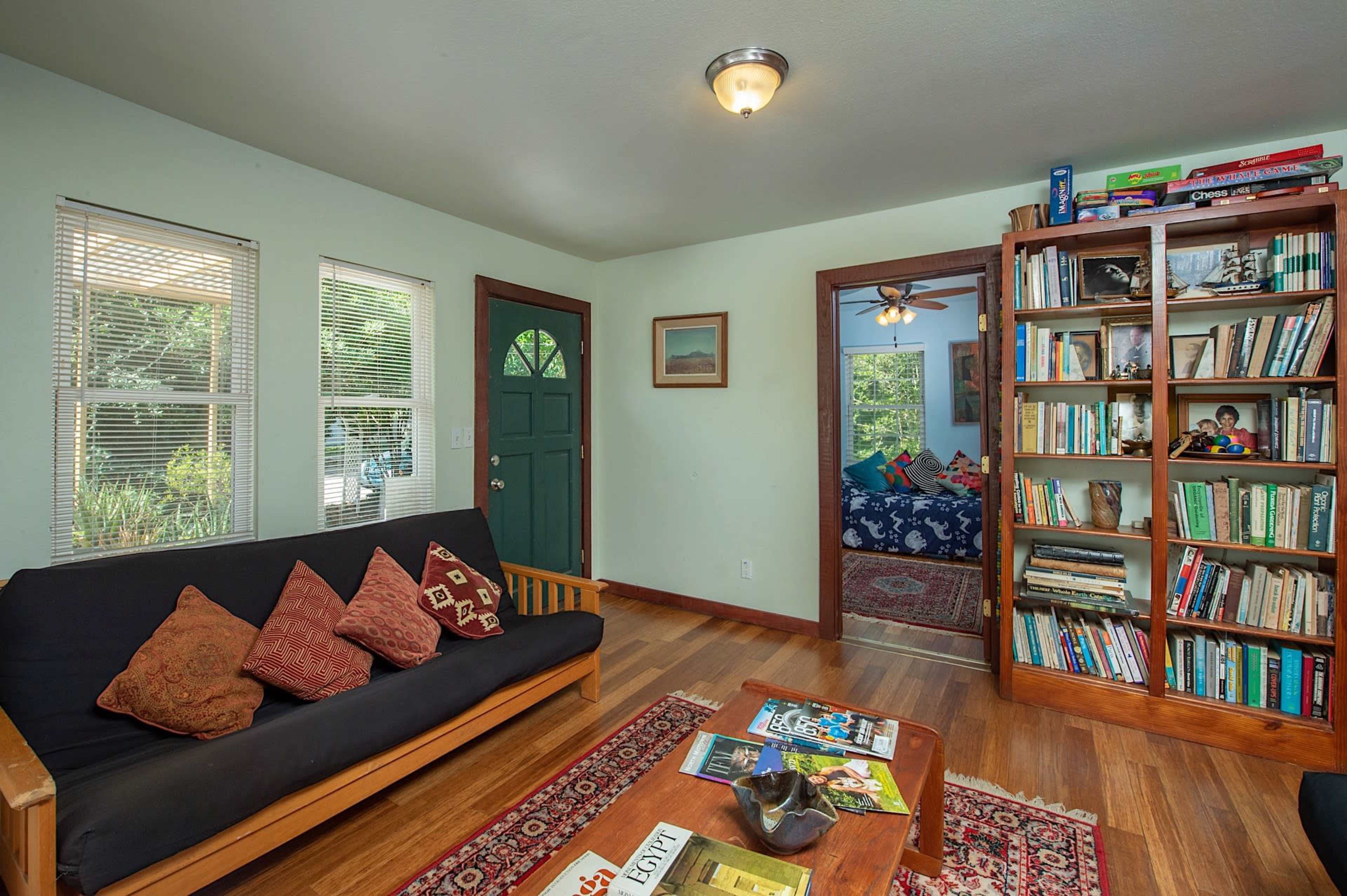 A cozy living room featuring a dark couch with patterned cushions, a wooden coffee table, and a bookshelf filled with books against a light green wall.