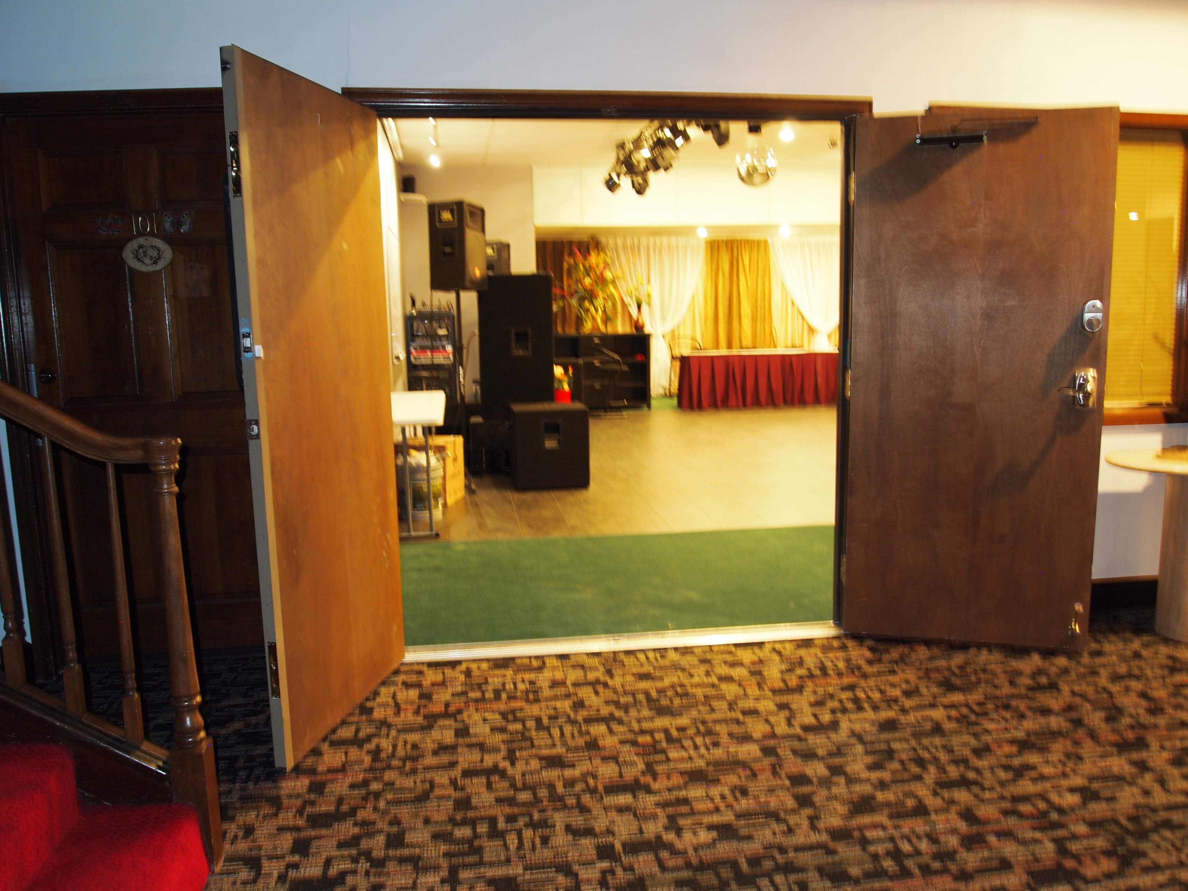 A set of double doors leading into a spacious, well-lit event room with musical equipment and a stage area in the background.