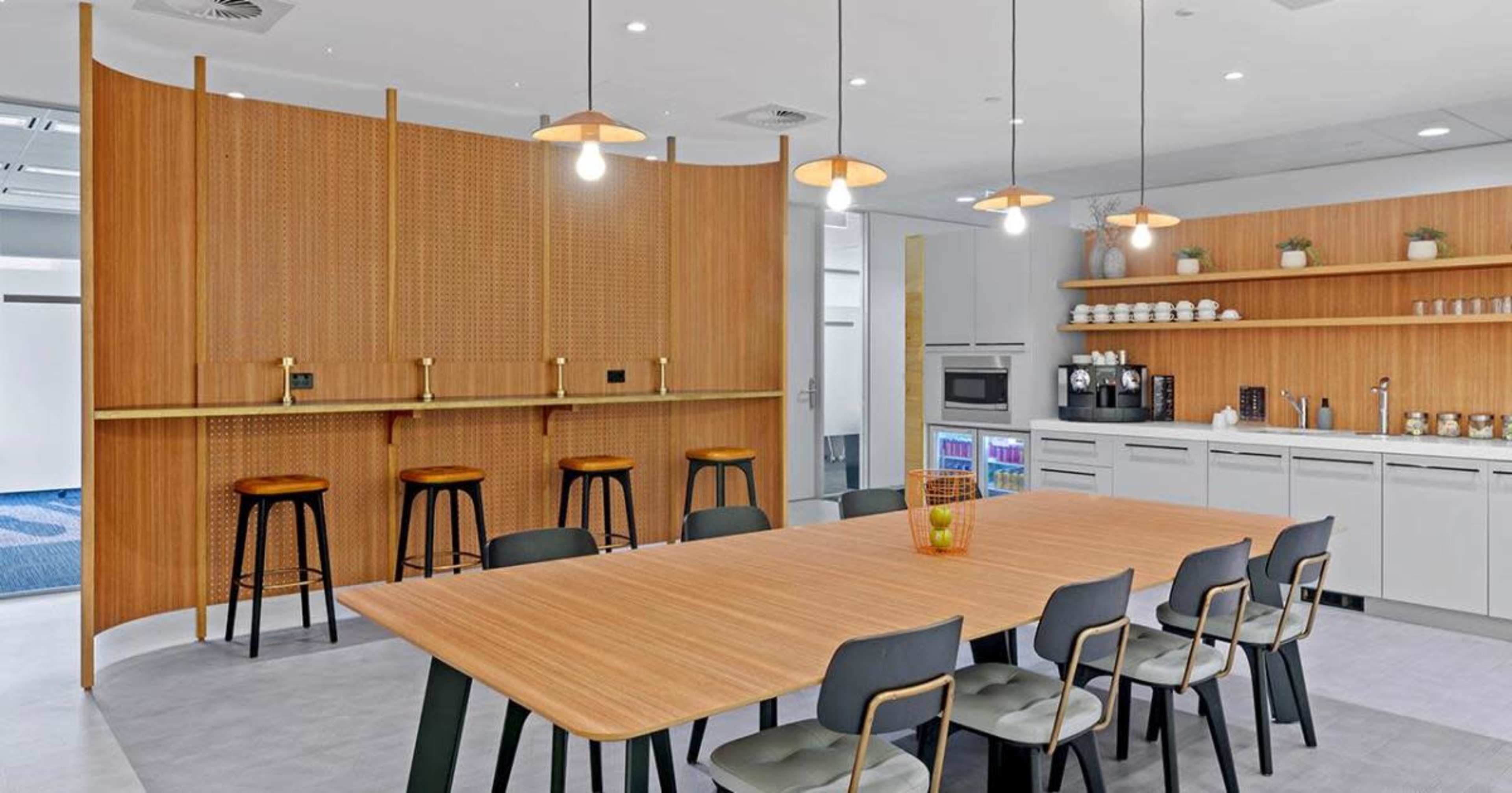 A modern kitchen and dining area featuring a wooden table with chairs, a bar with stools, and open shelving with kitchen appliances and decor.