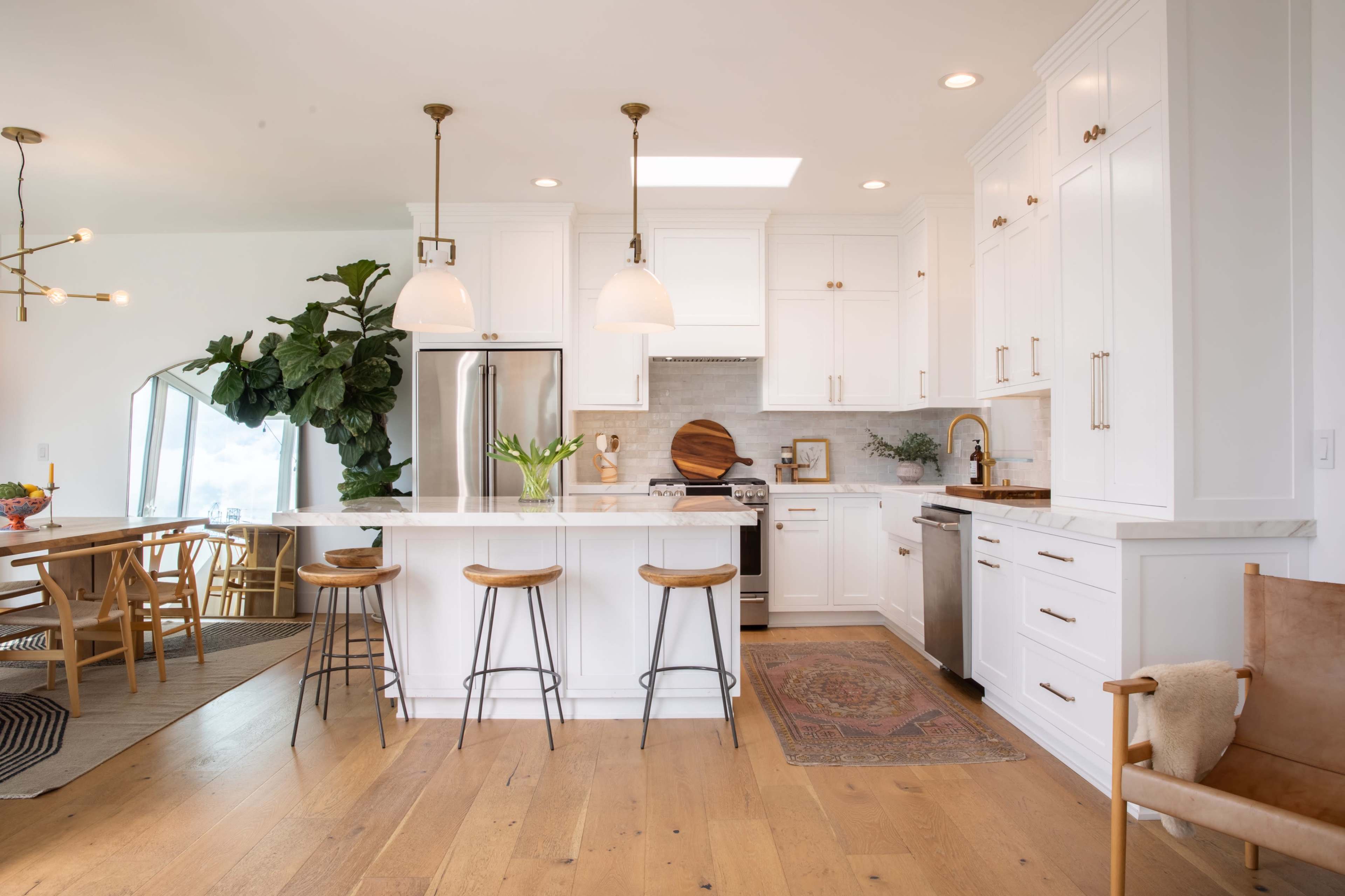 A modern kitchen featuring white cabinetry, a large island with three stools, and a dining area with a table and chairs nearby.