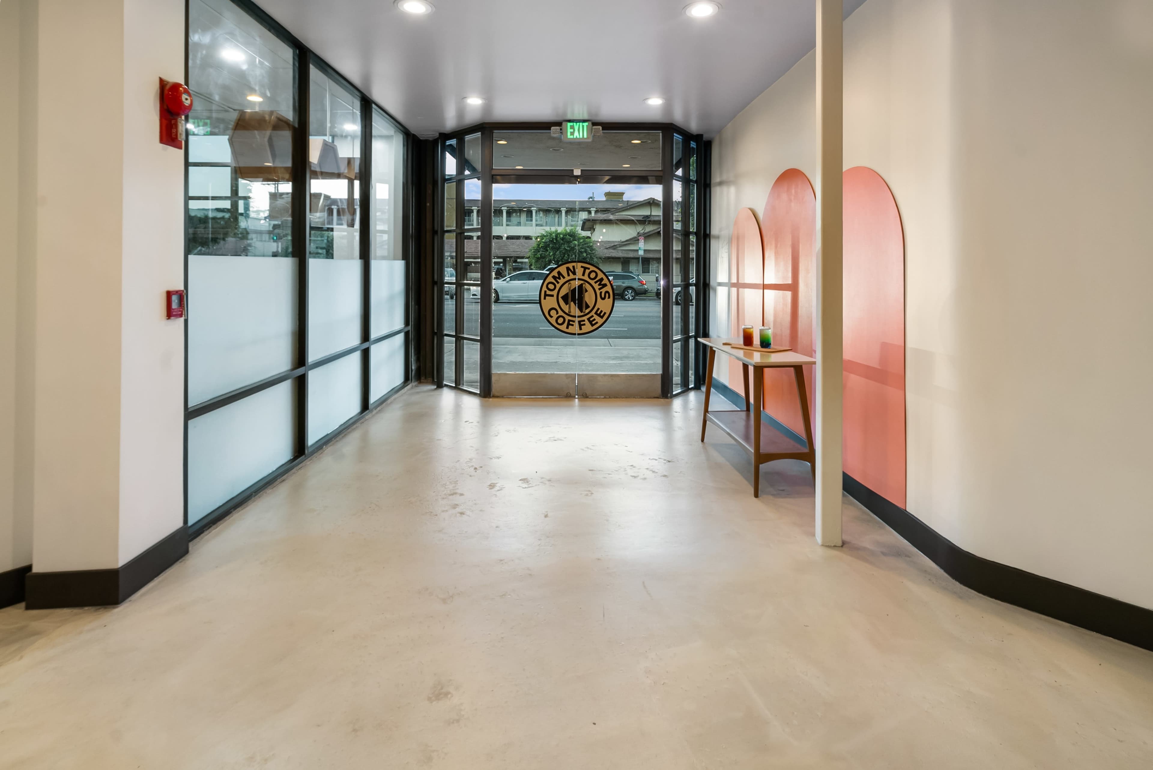 The interior entrance of a coffee shop with large glass doors, a light-colored floor, and a decorative wall featuring arched shapes.