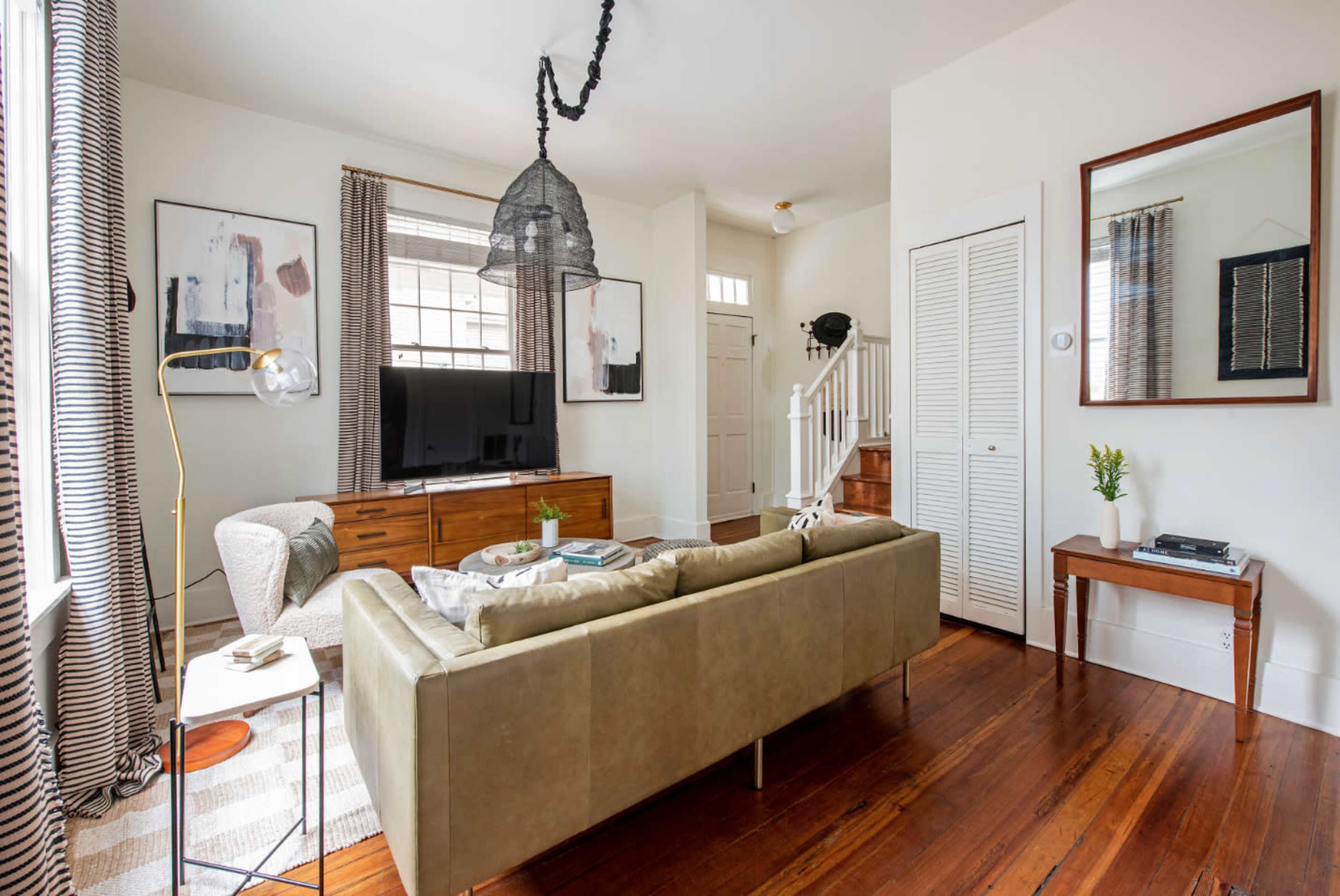The image shows a living room with a green sofa, a wooden TV stand, and a staircase leading to another level.
