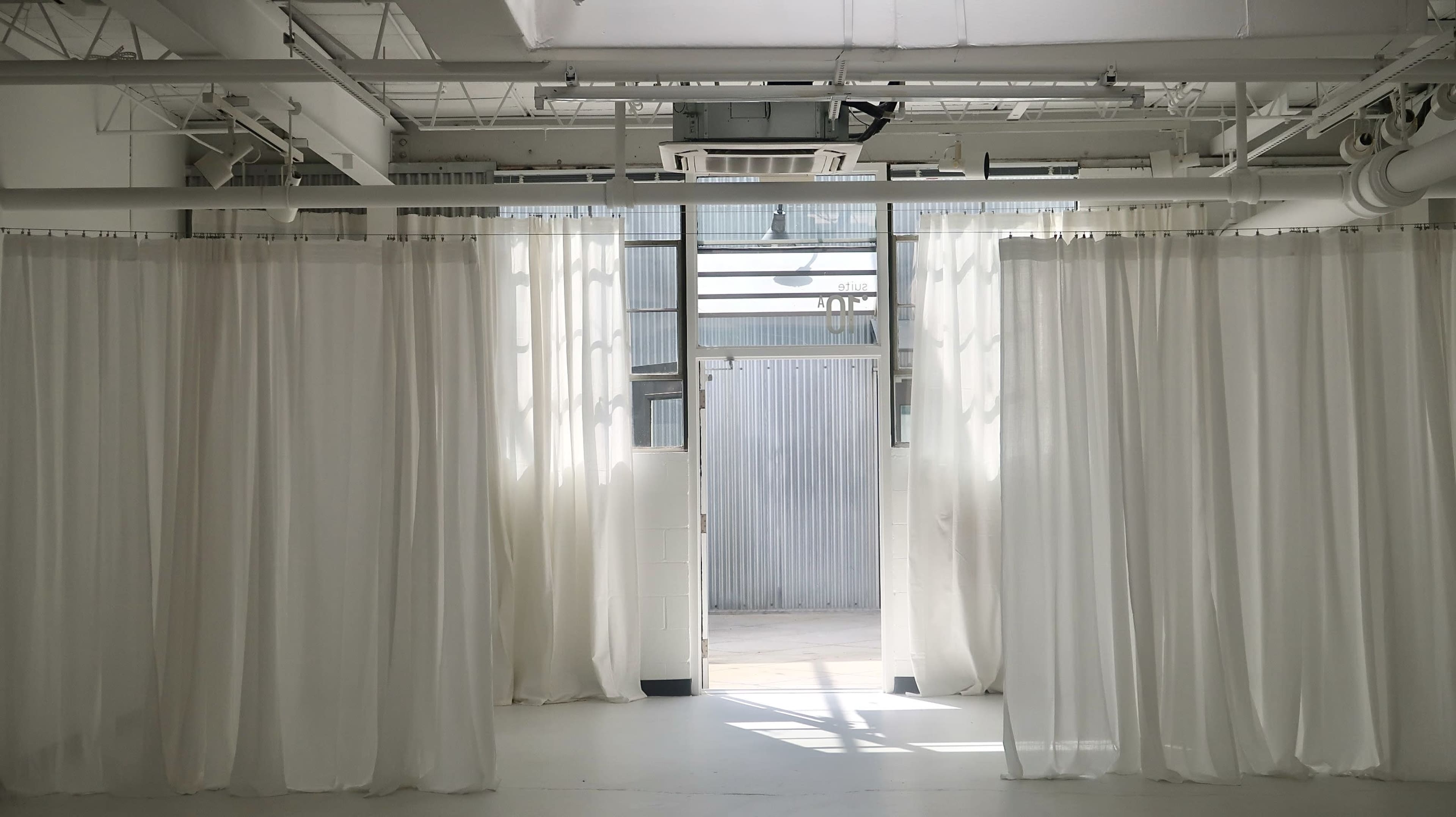 A spacious room with white curtains dividing areas and an open doorway leading to an outdoor space.
