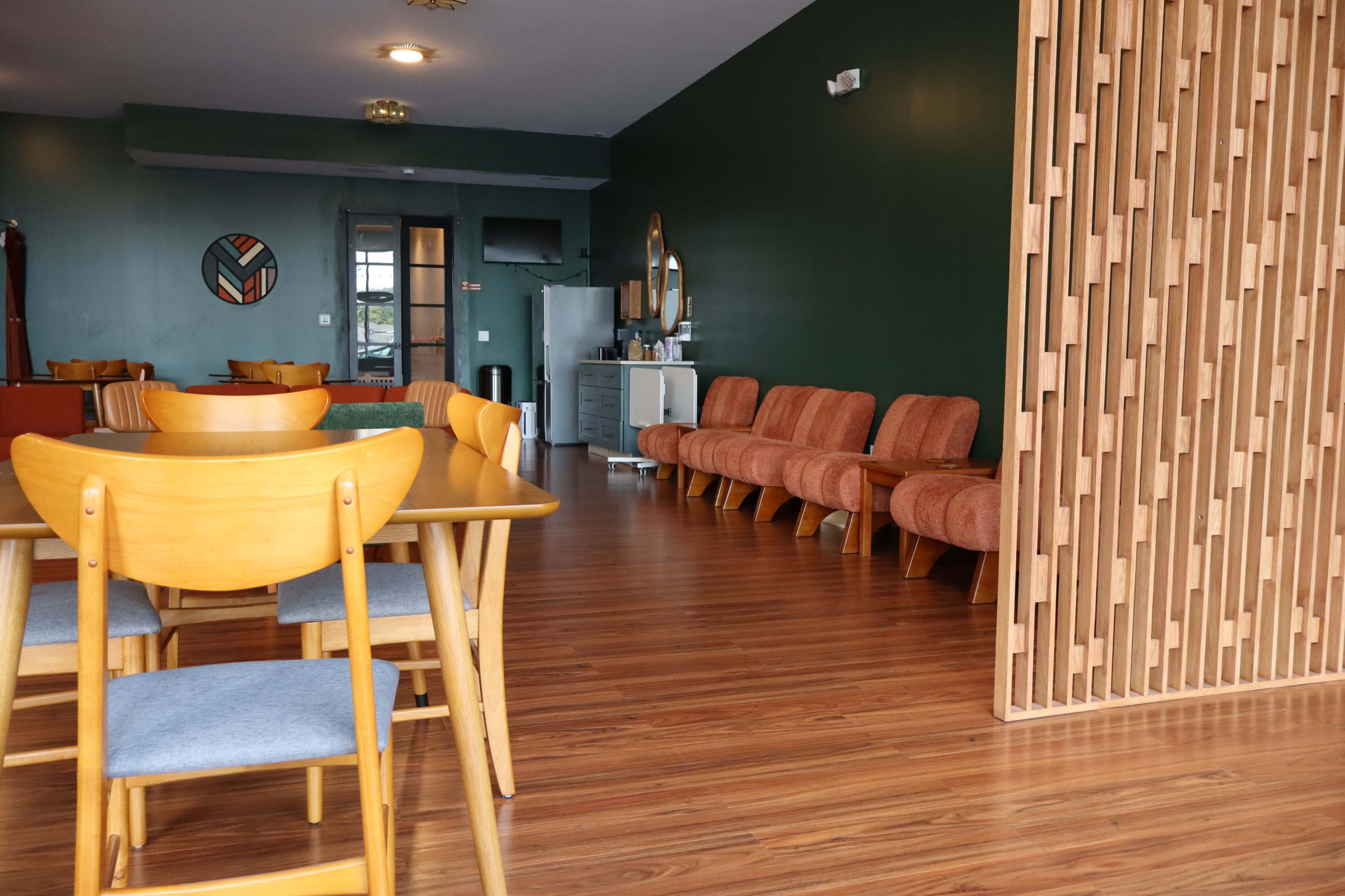 The image shows a modern interior space with wooden dining furniture, orange upholstered chairs, and a green accent wall.
