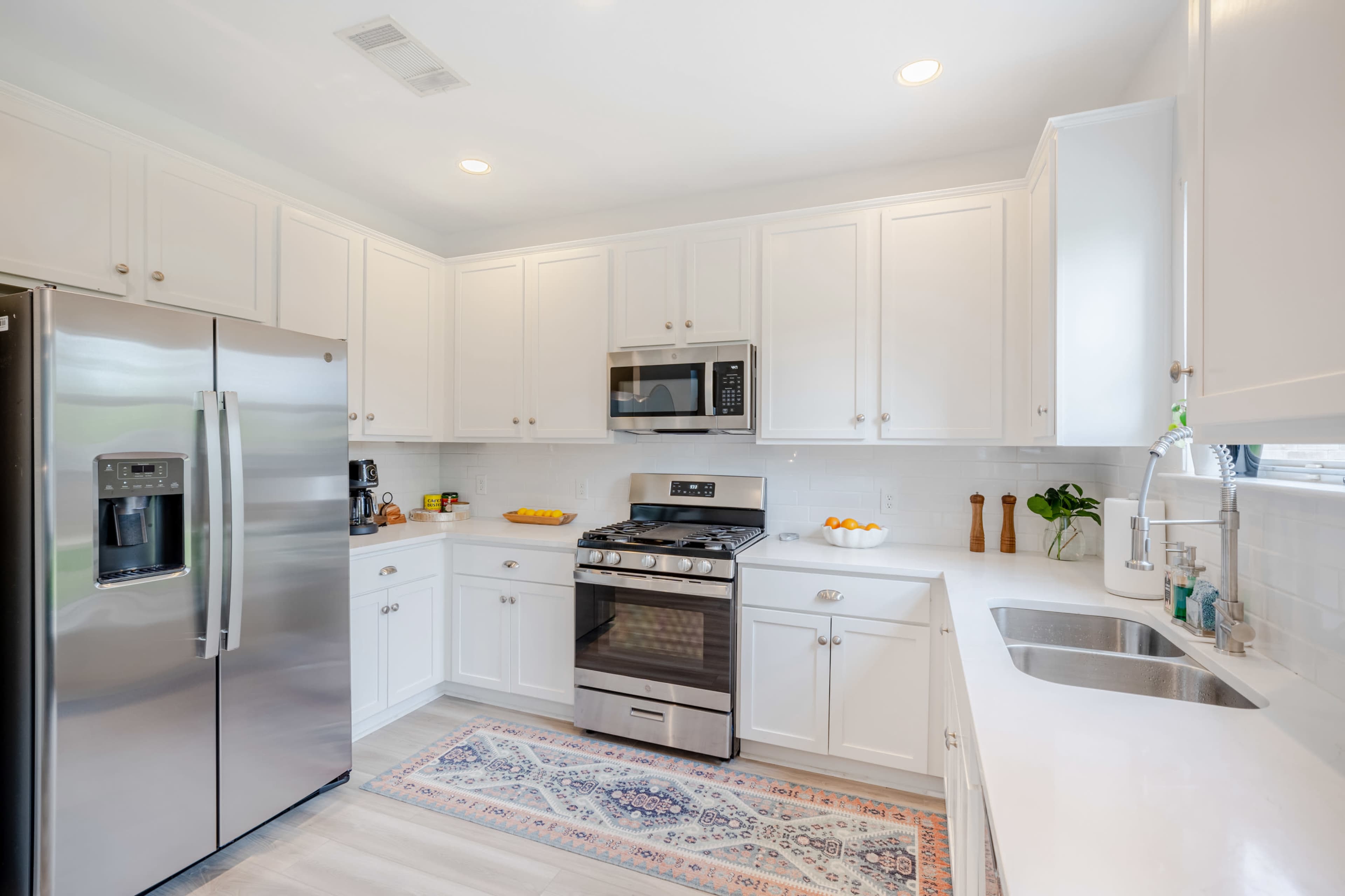 A modern kitchen with white cabinetry, stainless steel appliances, and a decorative rug on the floor.