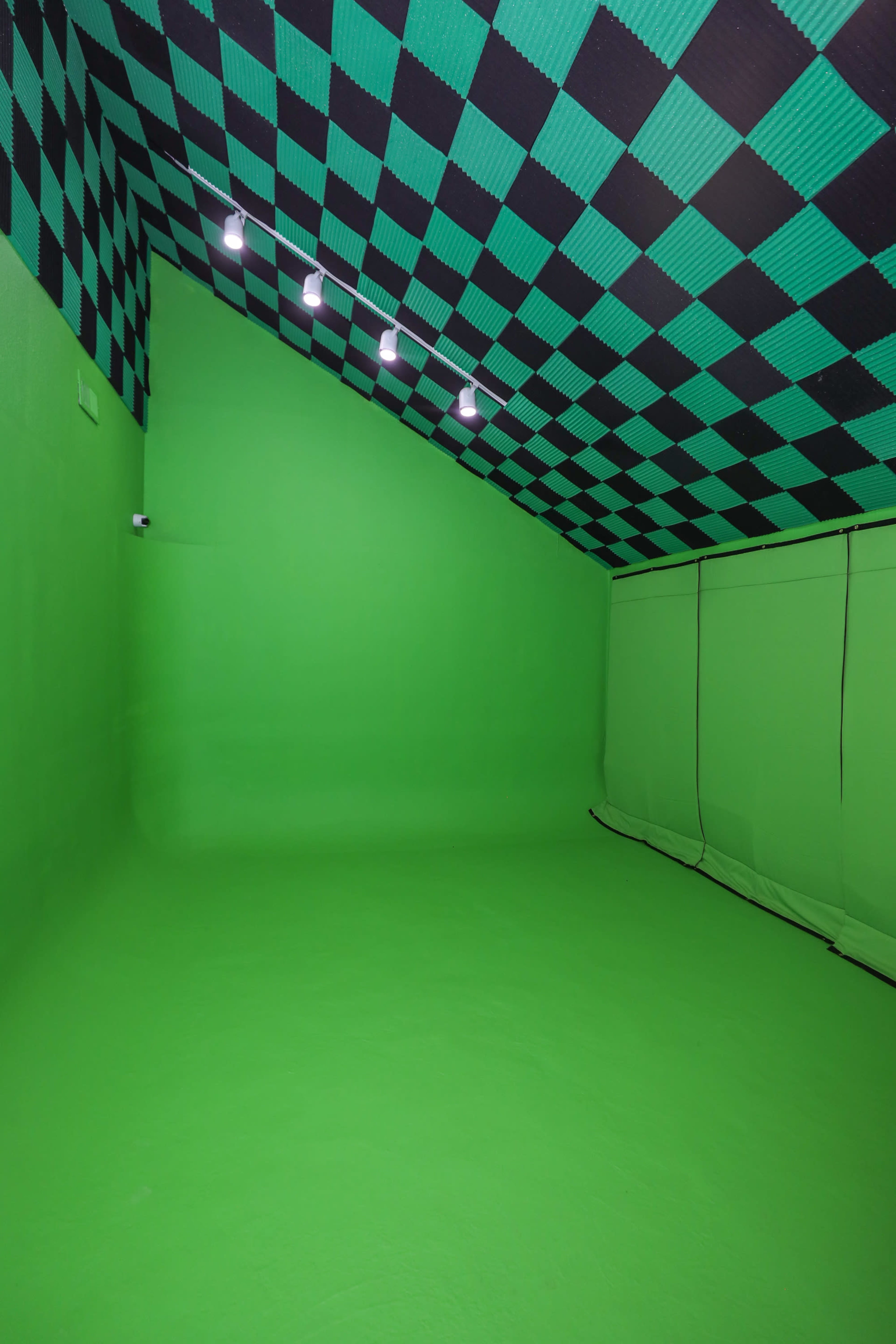 The image shows a green room with a black and green checkered ceiling and bright lights installed on it.