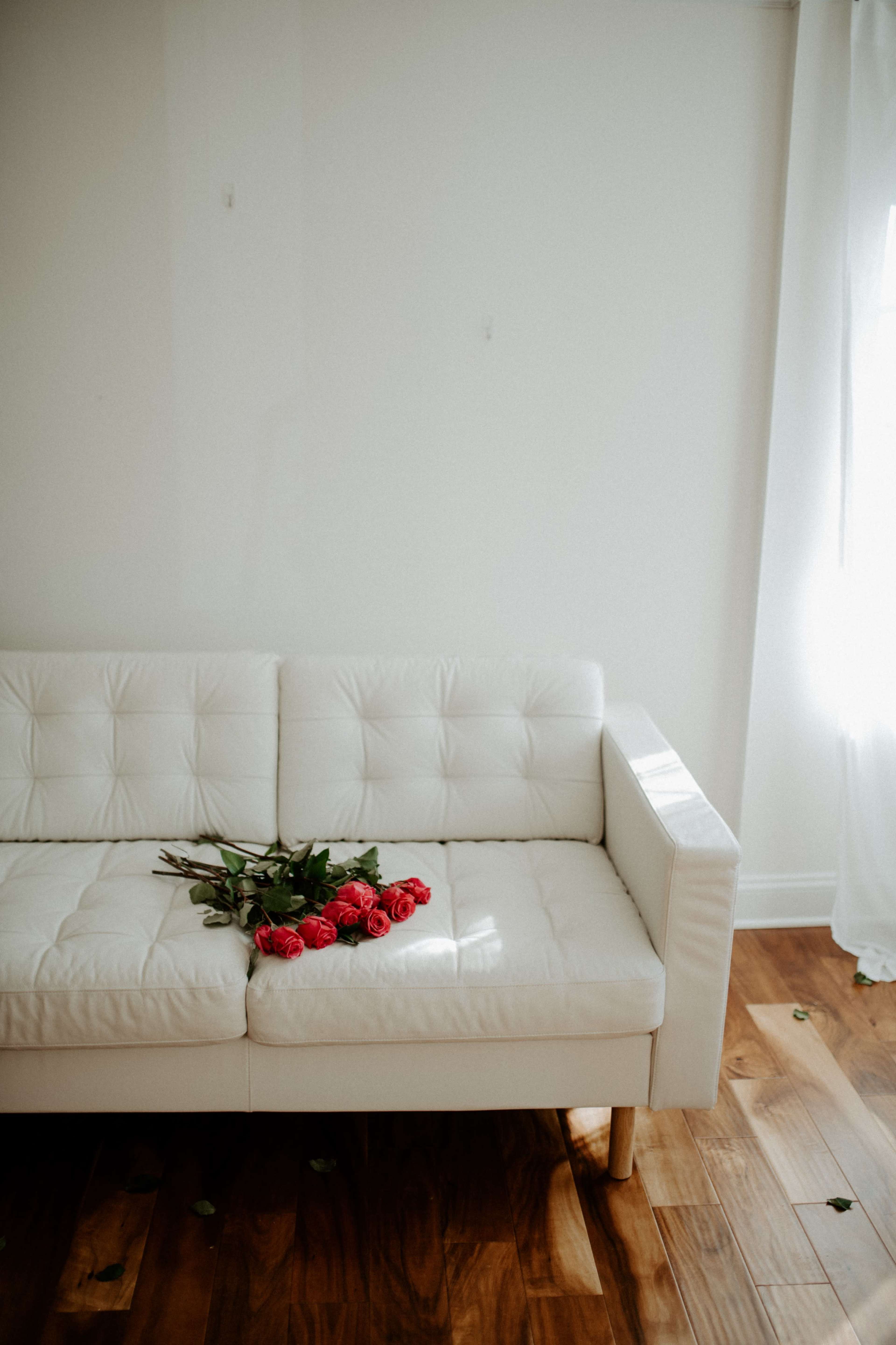 A white sofa is adorned with a bouquet of red roses, positioned against a plain wall in a well-lit room.