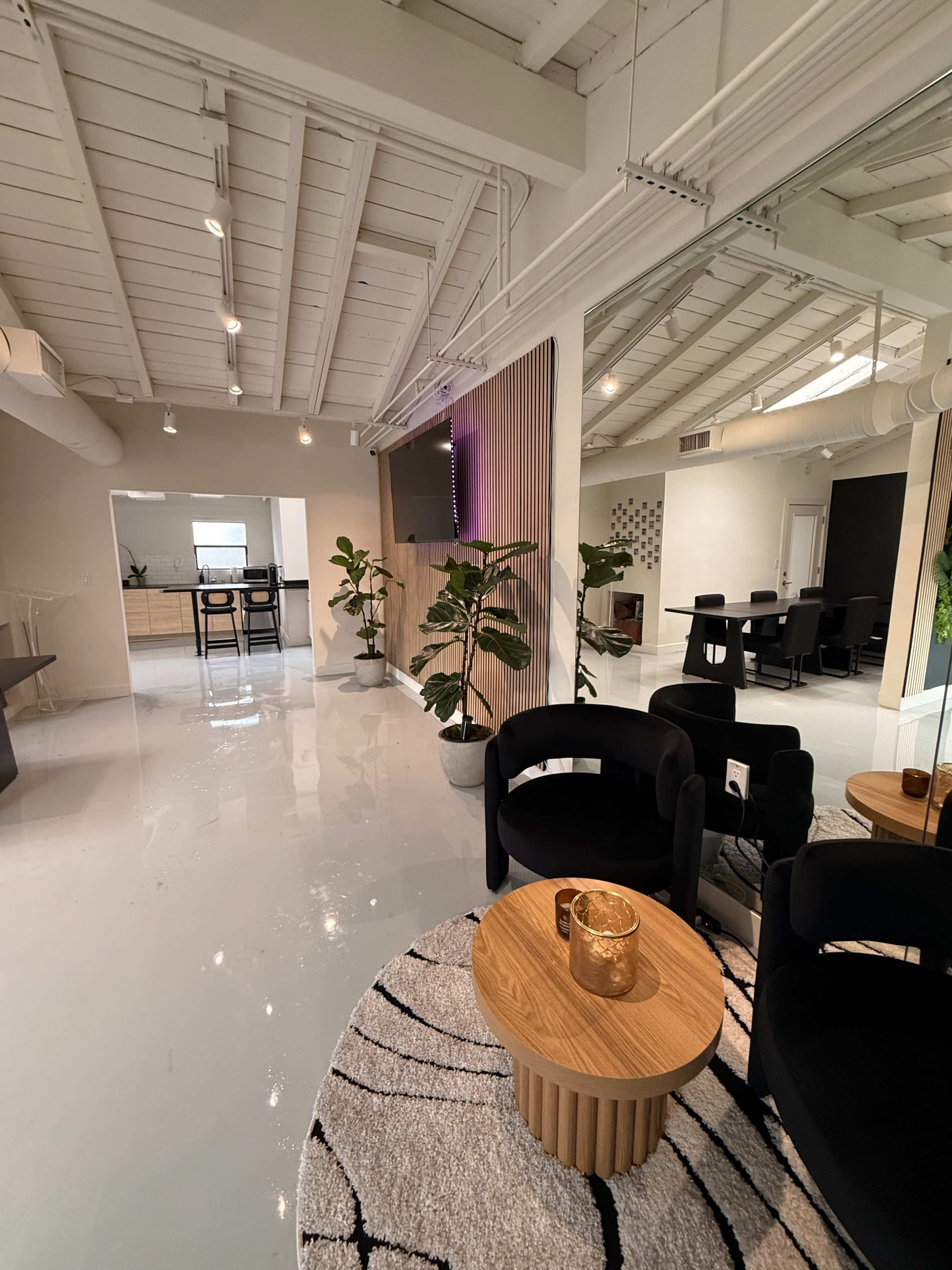 The image depicts a modern office space featuring sleek black chairs, a wooden table, plants, and a bright, polished floor.