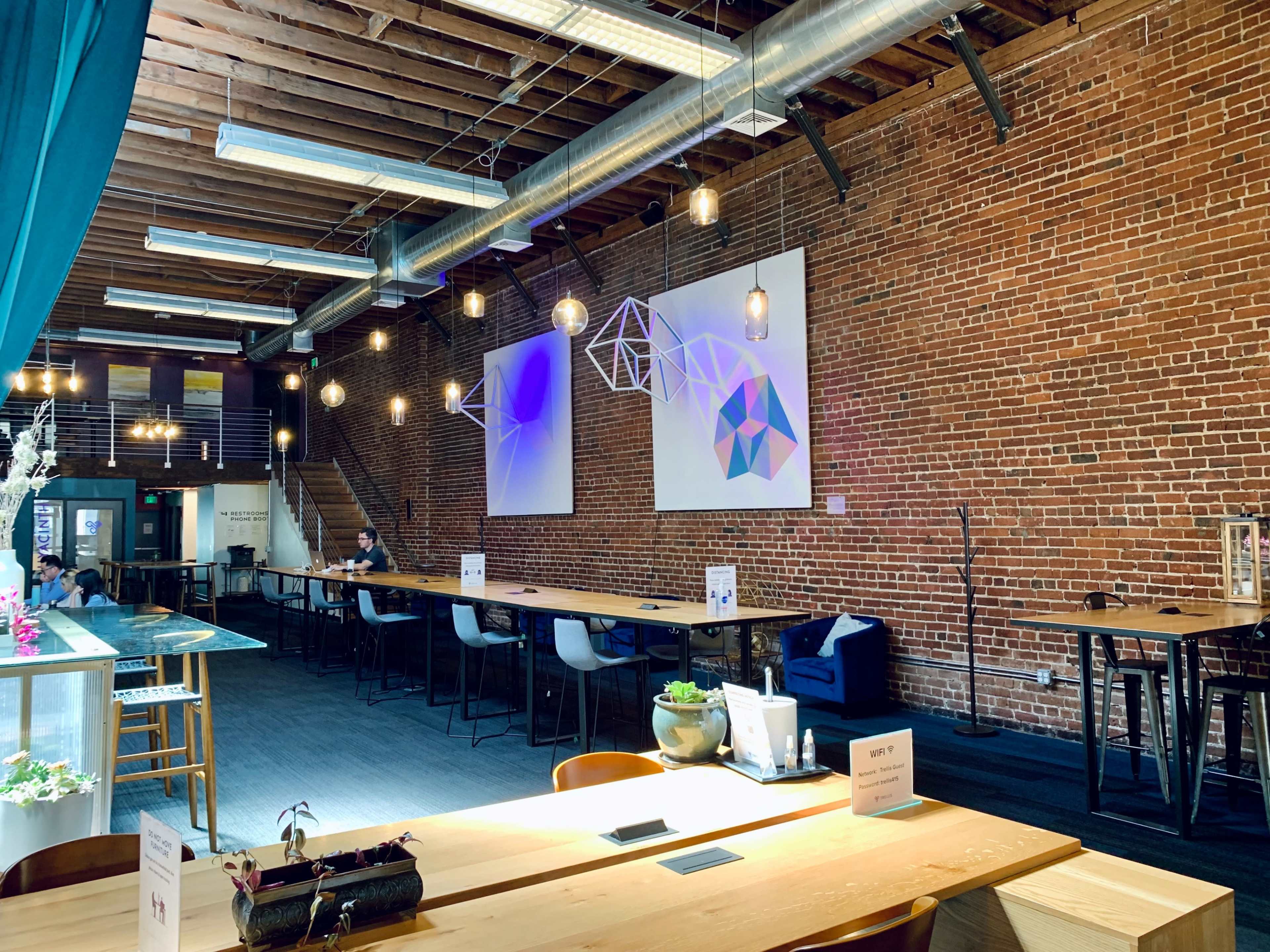 An open coworking space with exposed brick walls, large tables, and modern lighting fixtures.