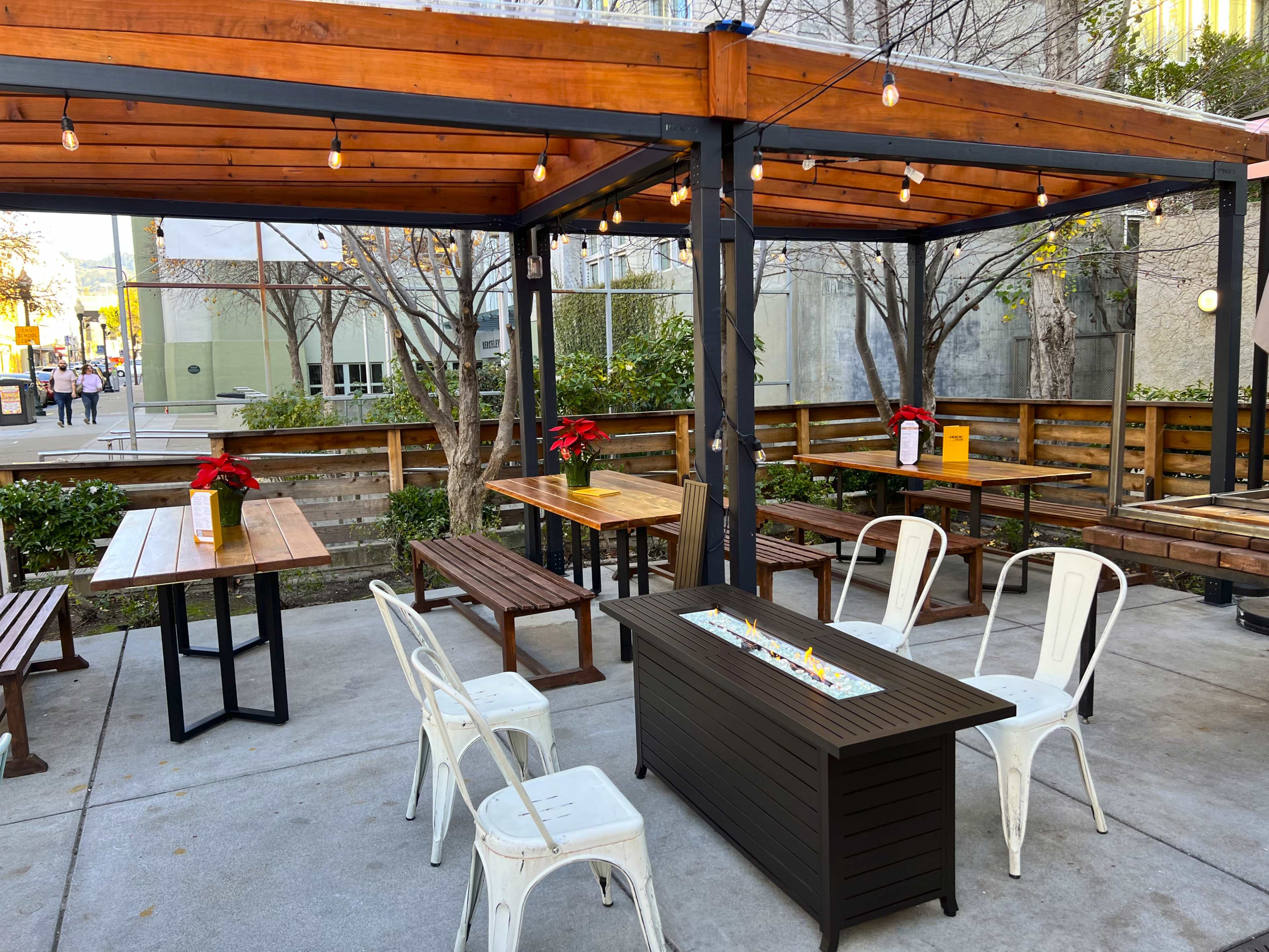 An outdoor dining area with wooden tables and chairs, surrounded by a wooden fence and string lights.