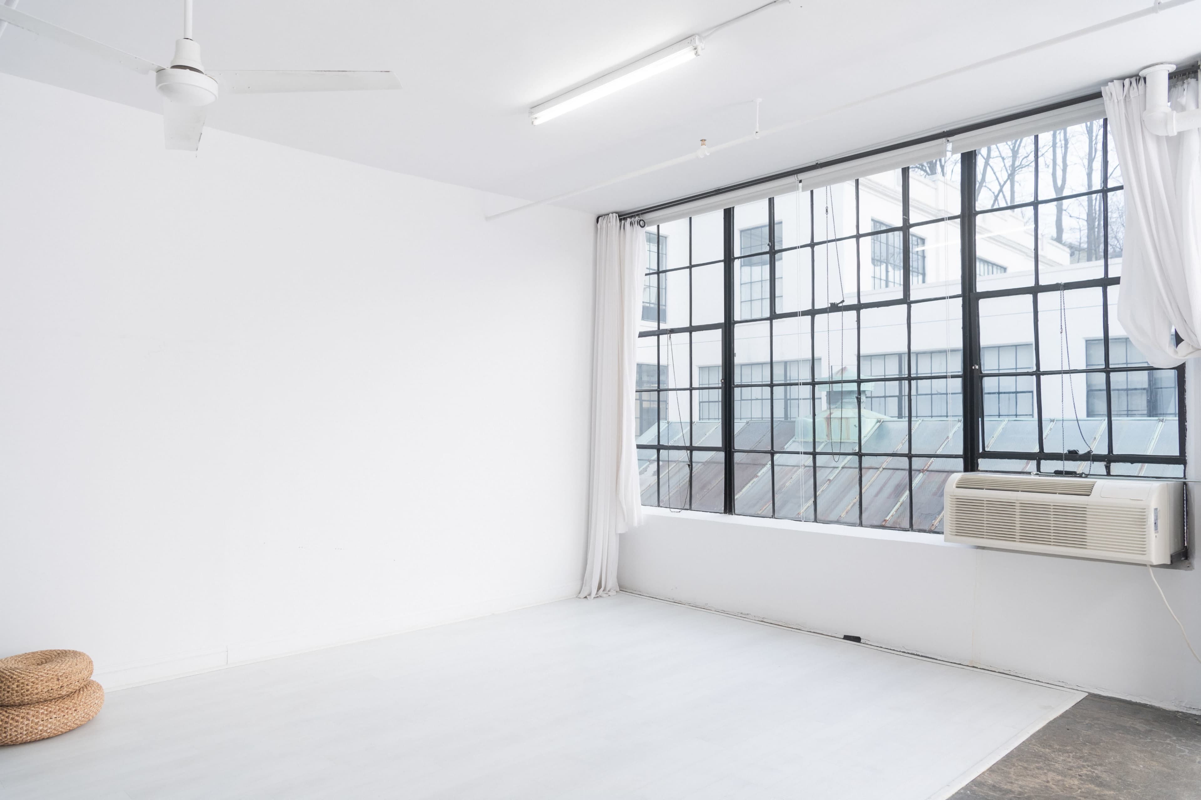 A minimalist, empty room with a large window and an air conditioning unit.