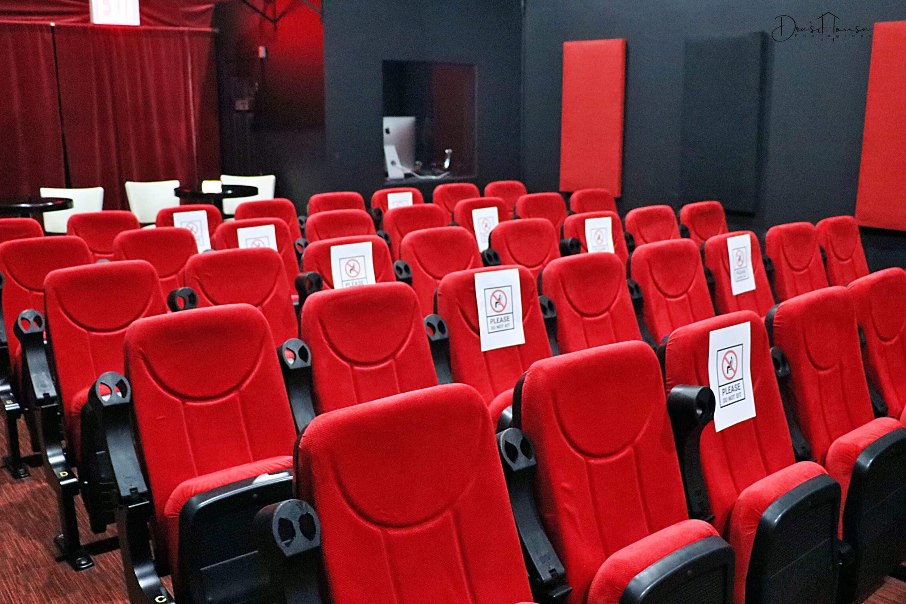 A row of red theater seats is marked with signs prohibiting the use of cell phones.