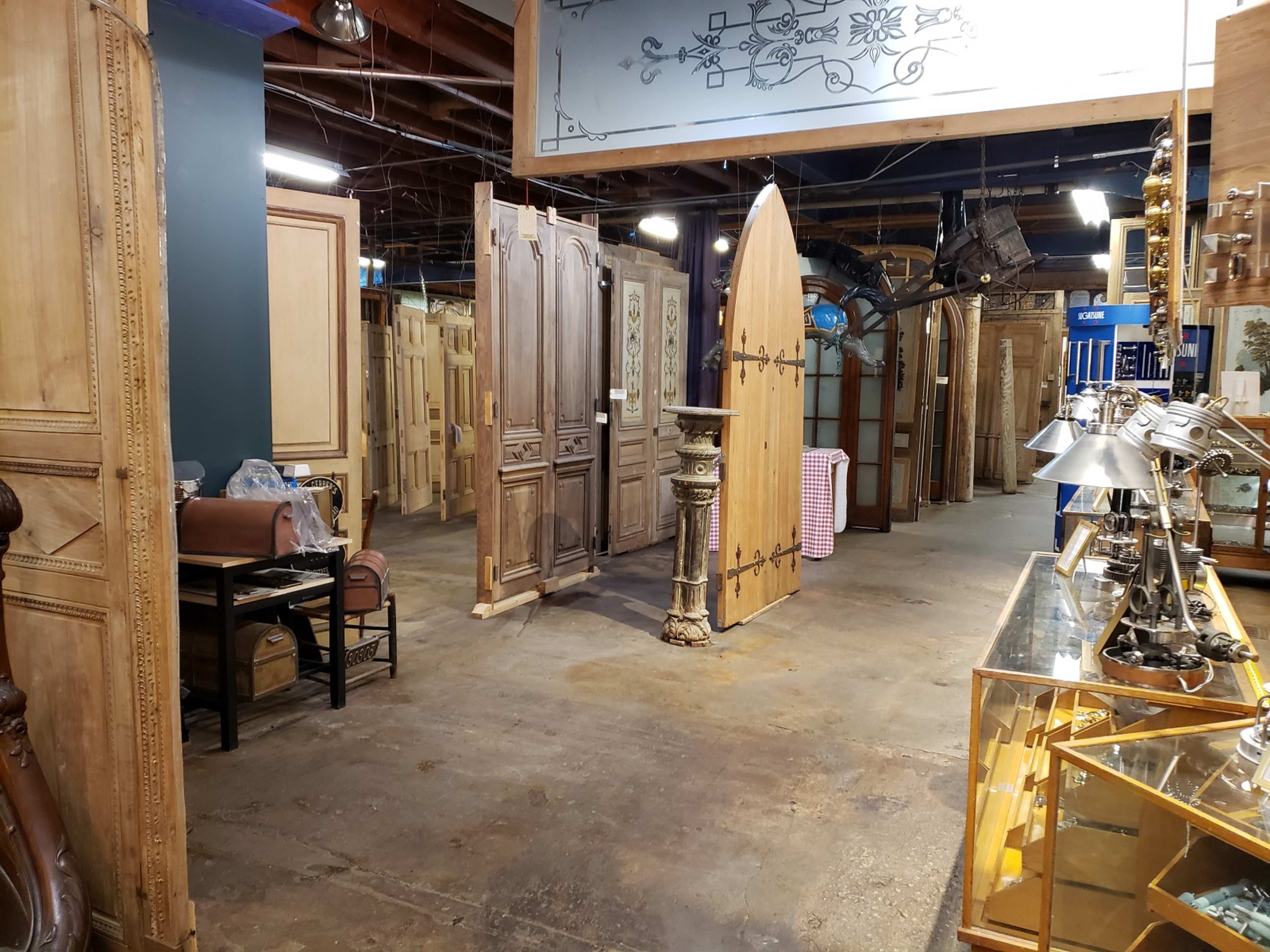 The image shows an interior space filled with various antique doors and furniture items arranged along the walls.