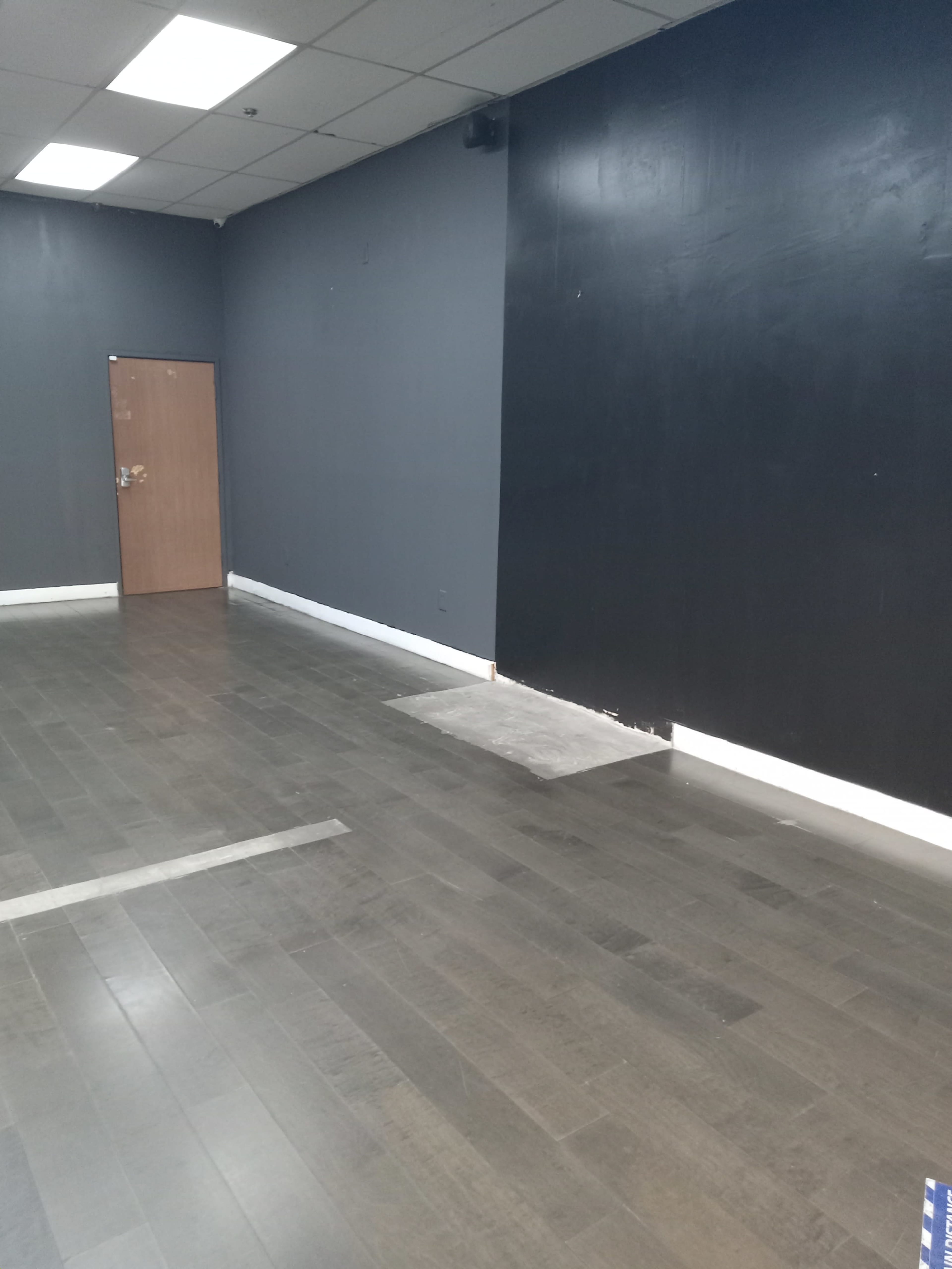 The image shows an empty room with dark walls, a wooden floor, and a door on one side.