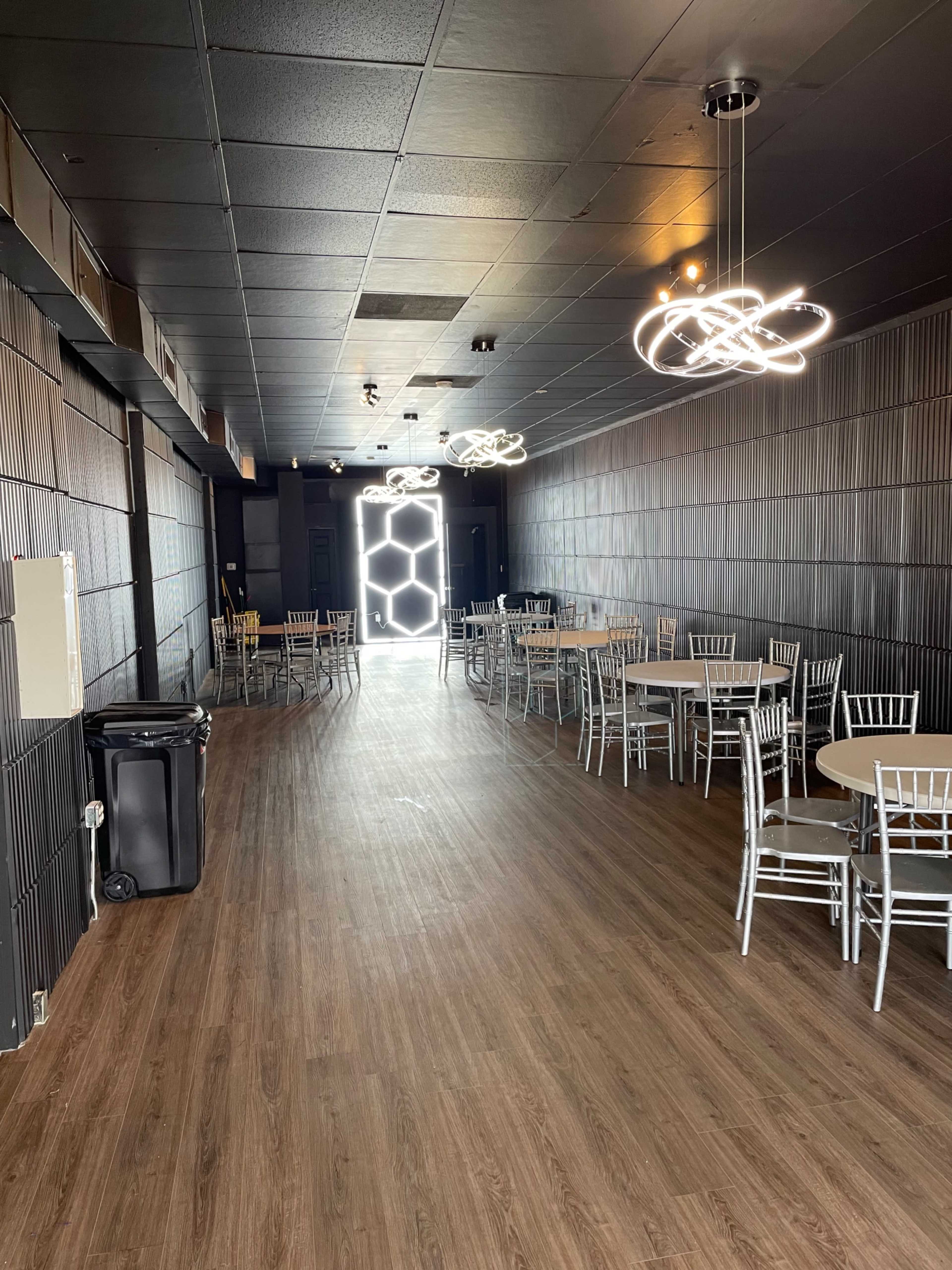 A spacious, empty indoor event room with several round tables and modern light fixtures.