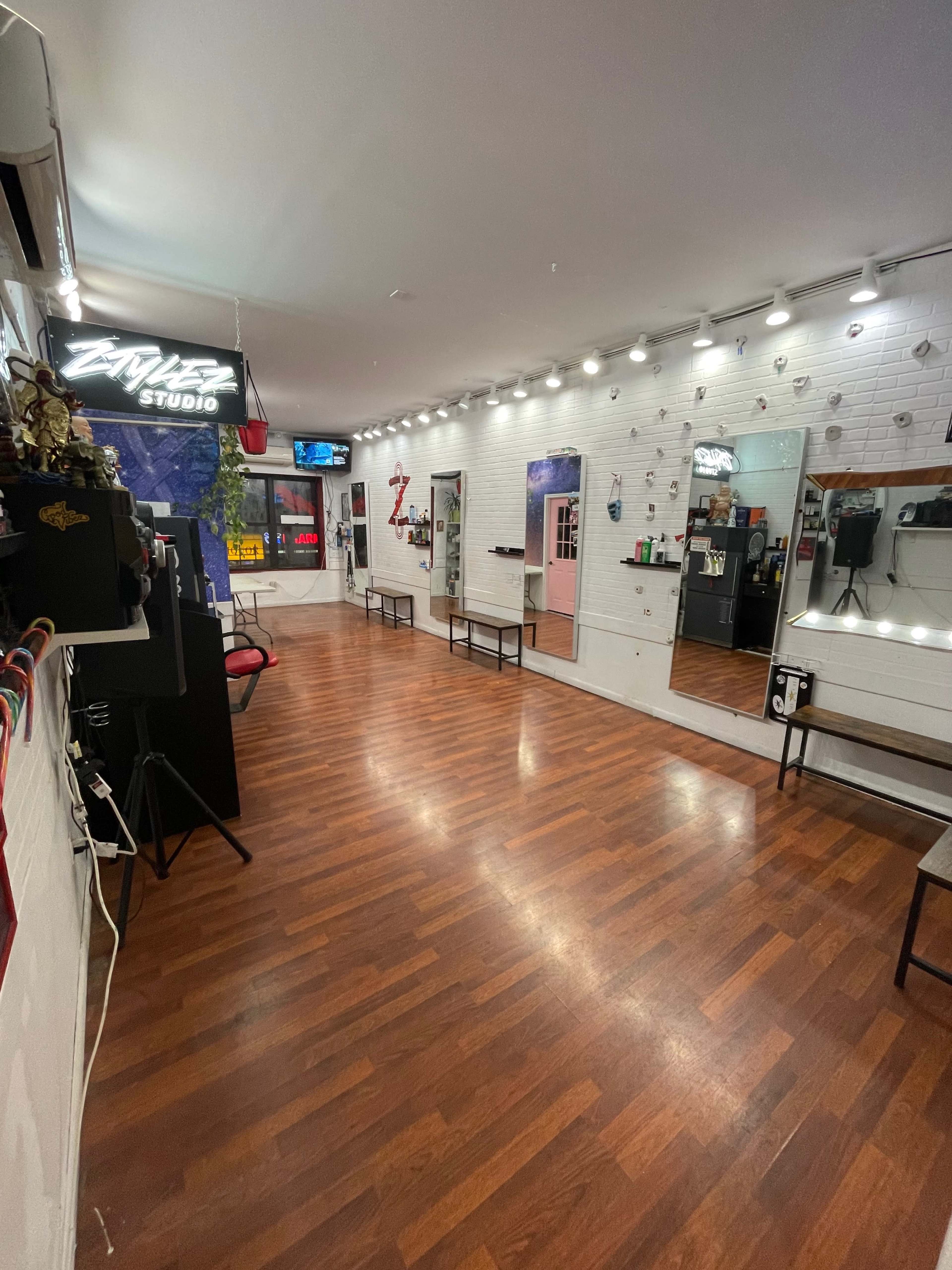 The image shows a spacious, well-lit studio with wooden floors and several mirrors along the walls.