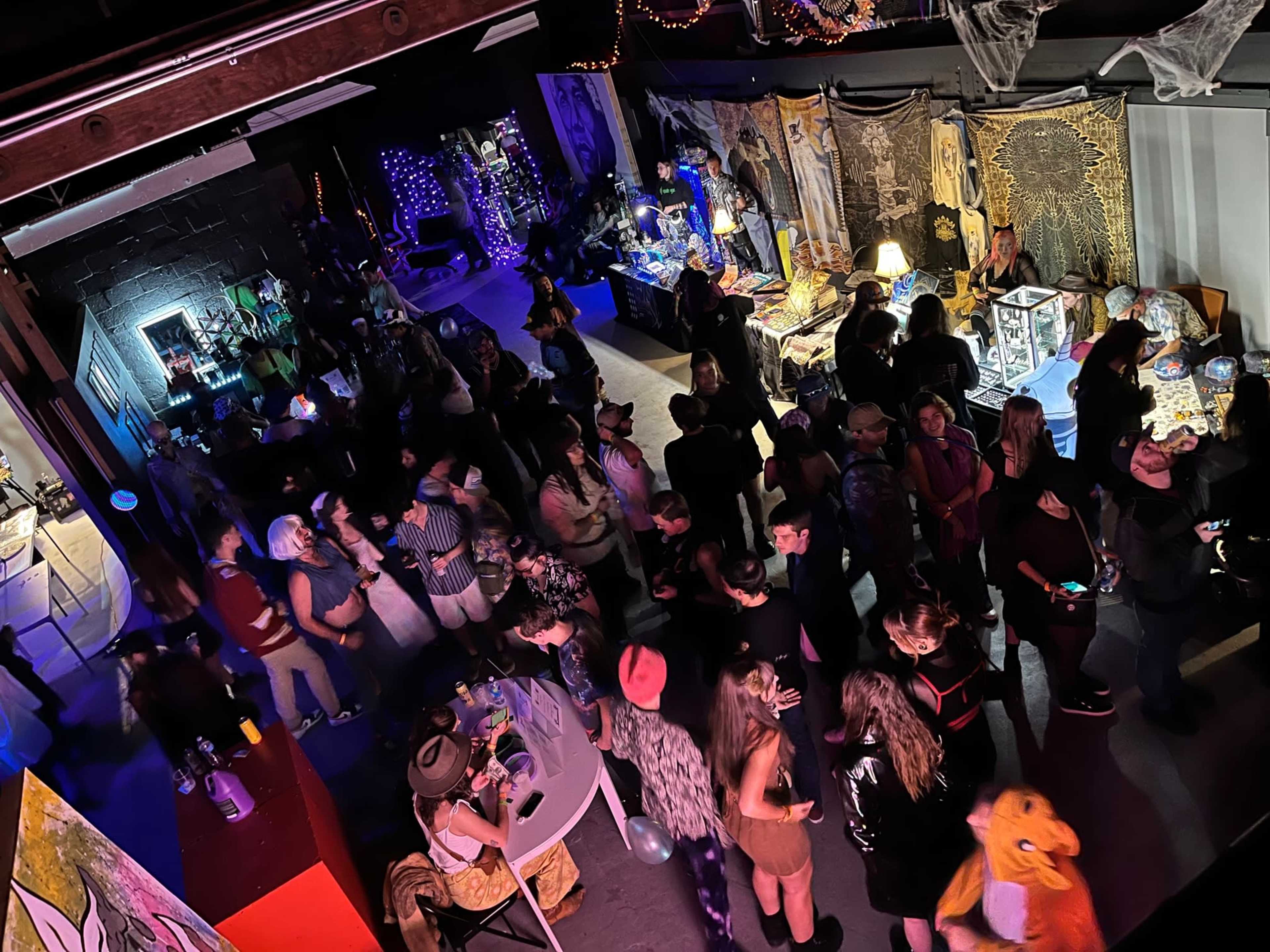 A crowded indoor venue features various decorations and people engaged in conversation, with booths set up in the background.