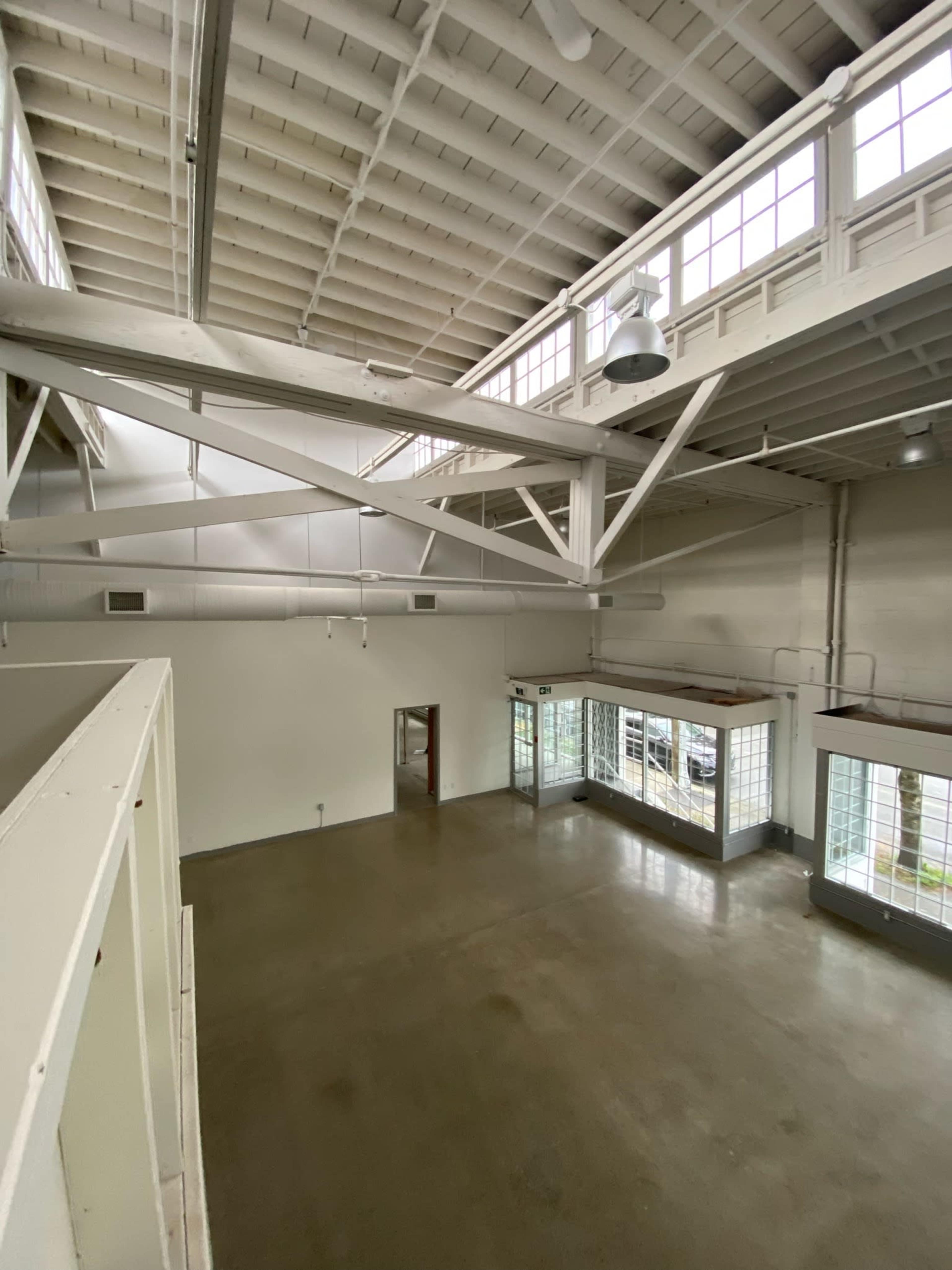 A spacious, industrial-style room with large windows and exposed beams.