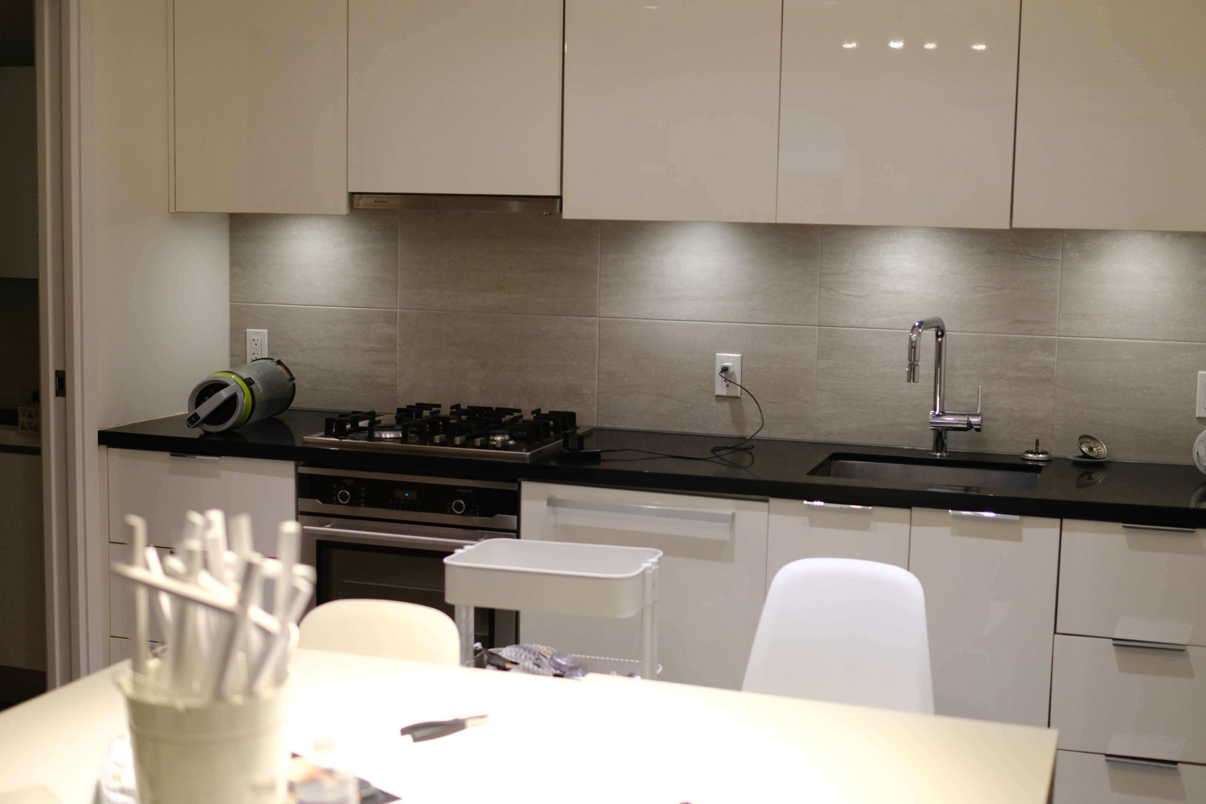 A modern kitchen with a gas stove, a stainless steel sink, and sleek cabinetry illuminated by under-cabinet lighting.