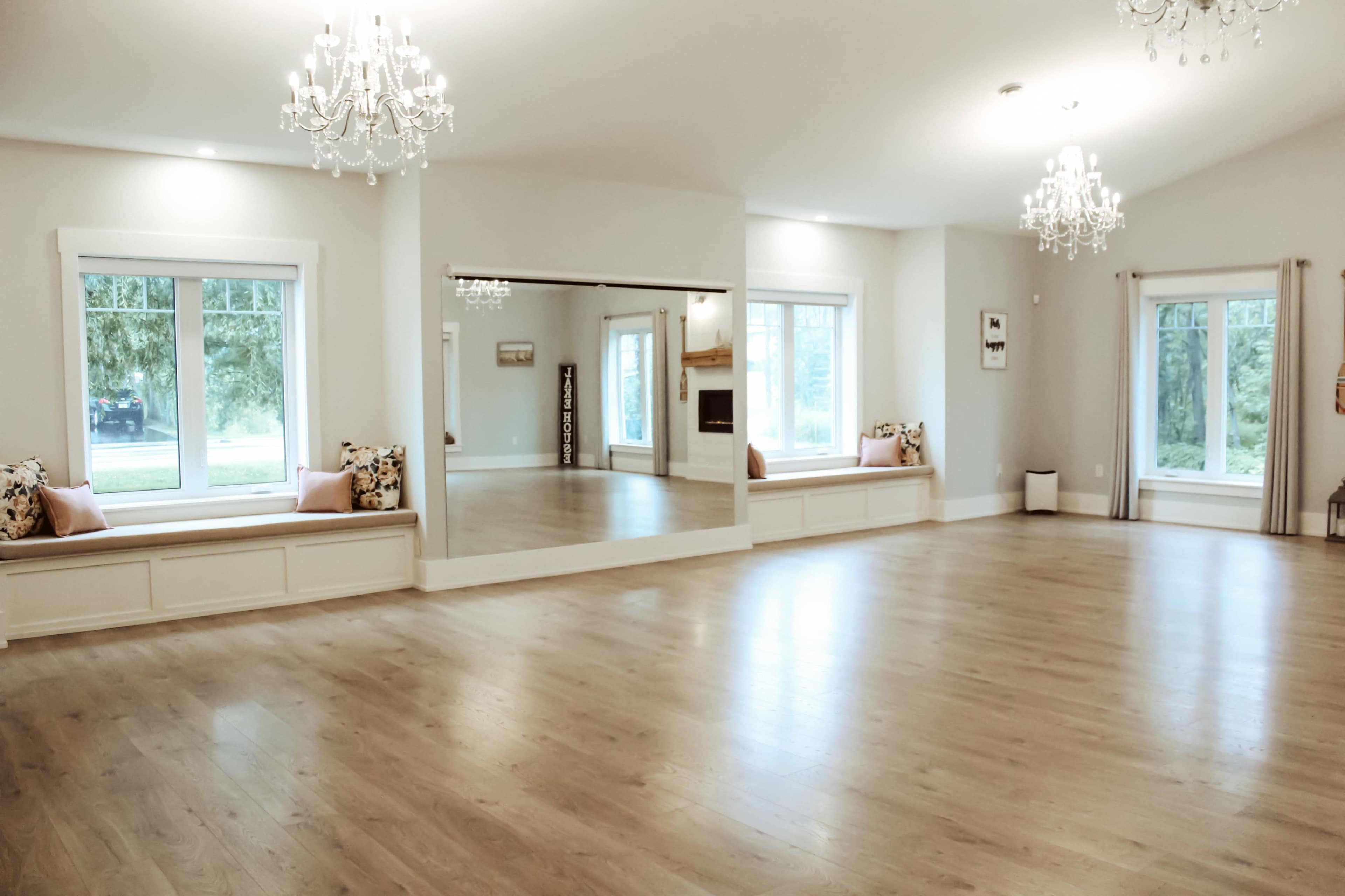 A spacious interior room with wooden flooring, large windows, mirror walls, and two decorative seating areas with cushions.