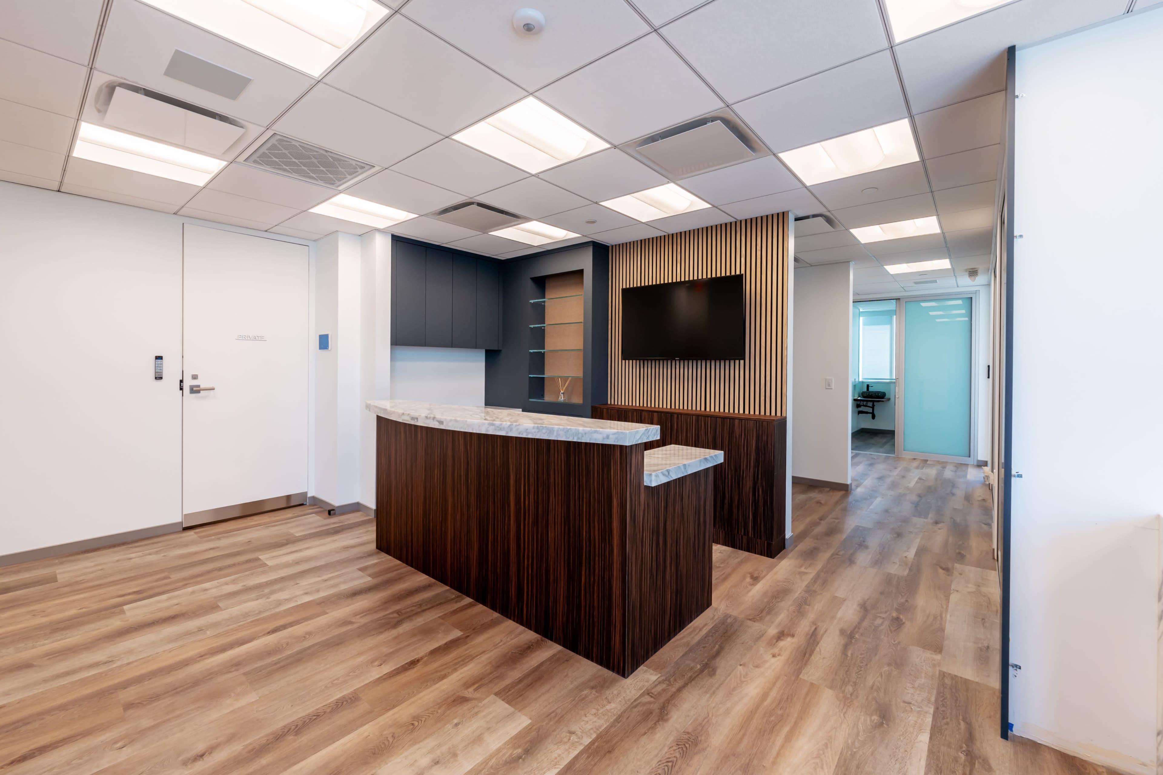 A modern office reception area with a wooden reception desk, gray cabinetry, and a television mounted on a wall.