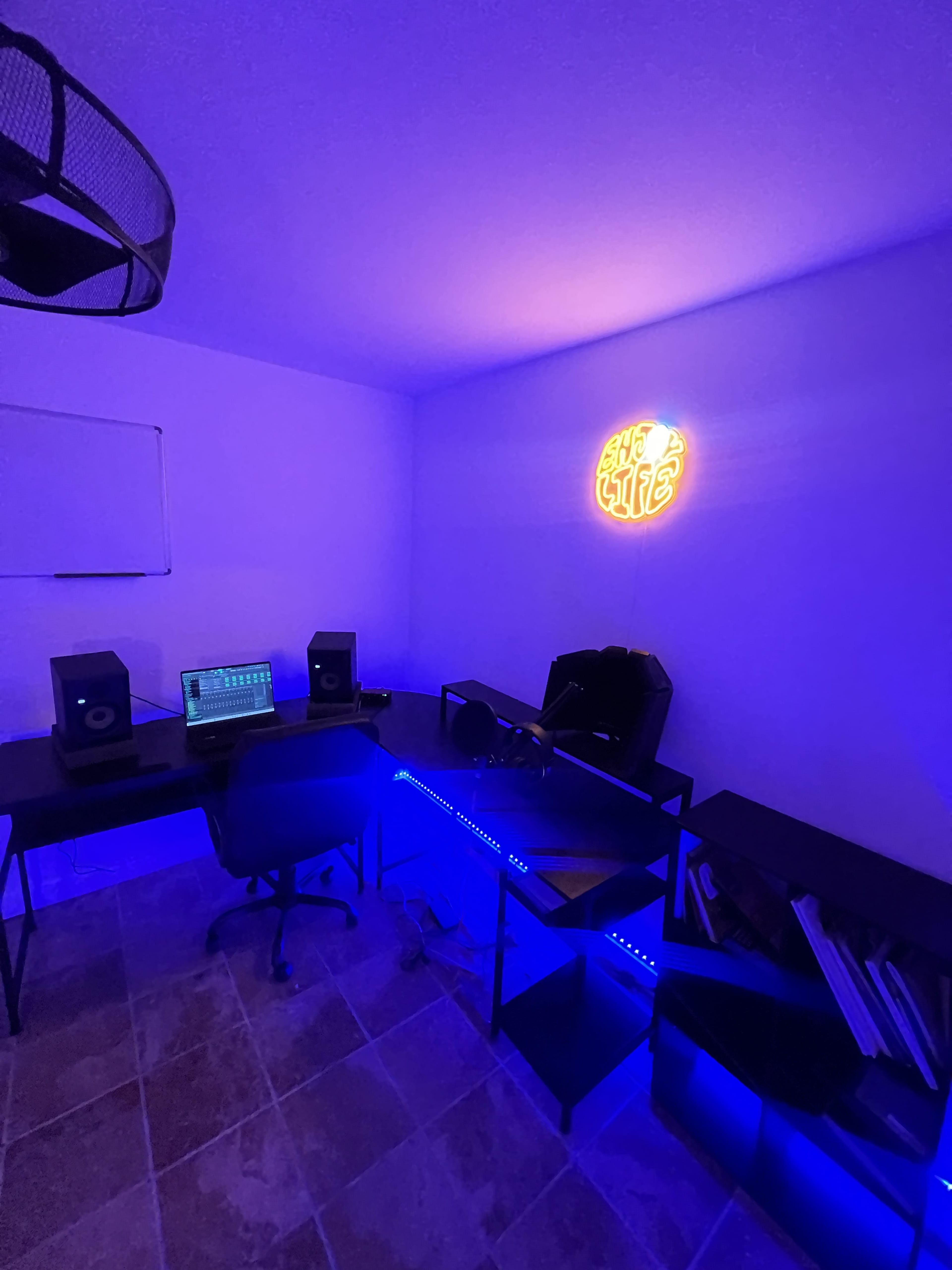 A modern workspace featuring two desks, a laptop with audio speakers, and neon lighting along the walls.