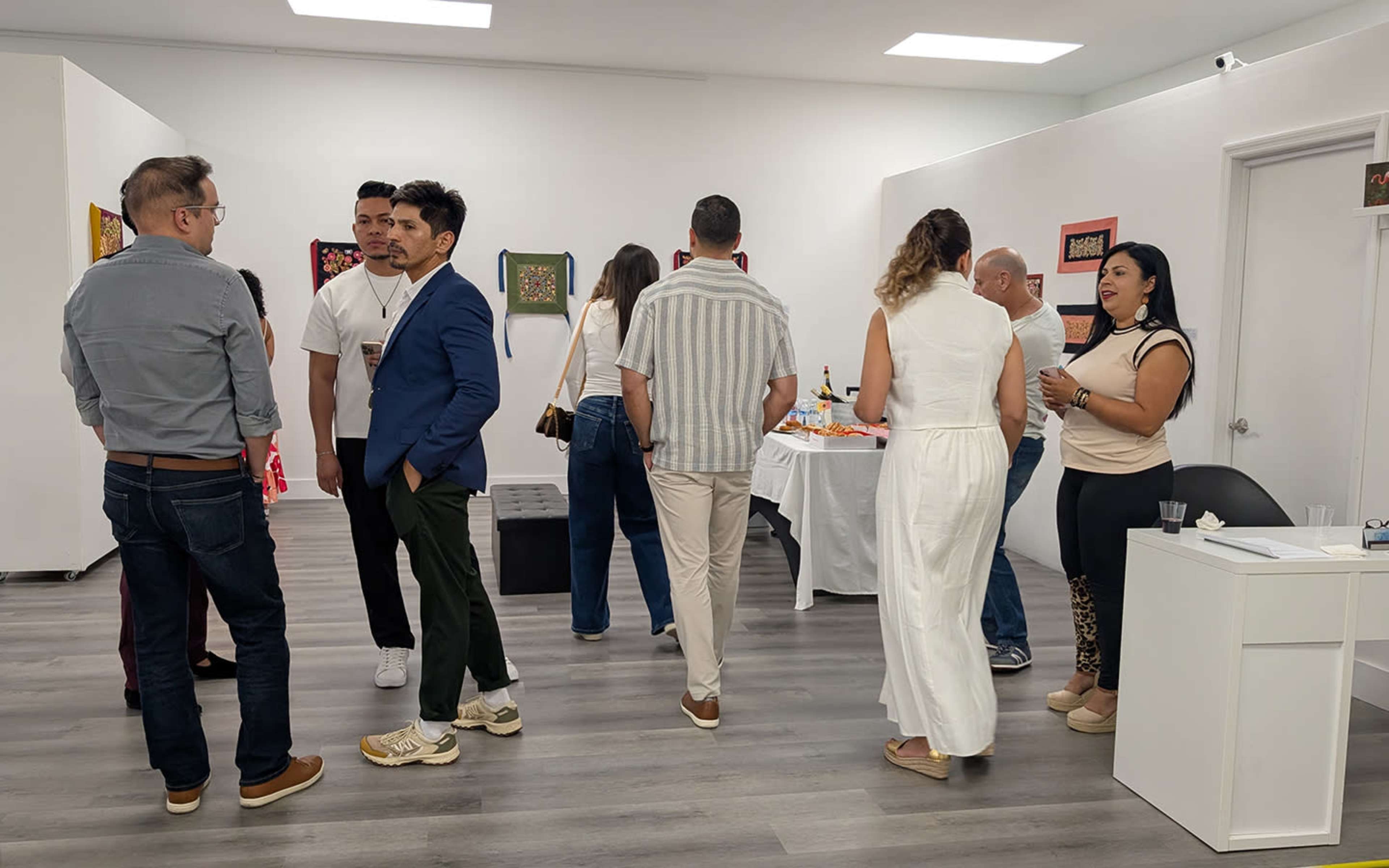 A group of people are gathered in an art gallery, engaging in conversation while displaying various artworks on the walls.
