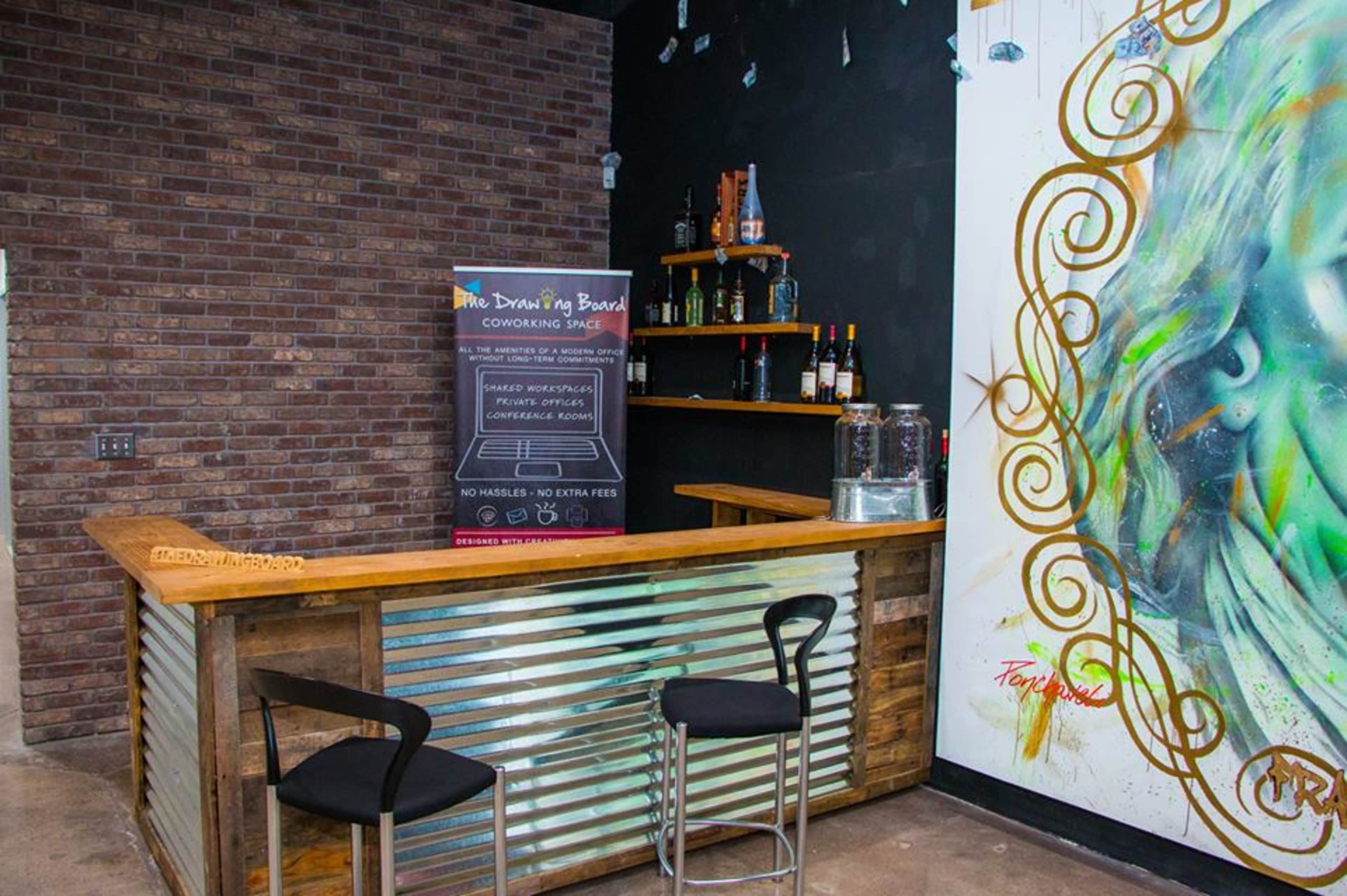 A rustic bar area with a wooden counter, metal accents, and a wall featuring colorful artwork.