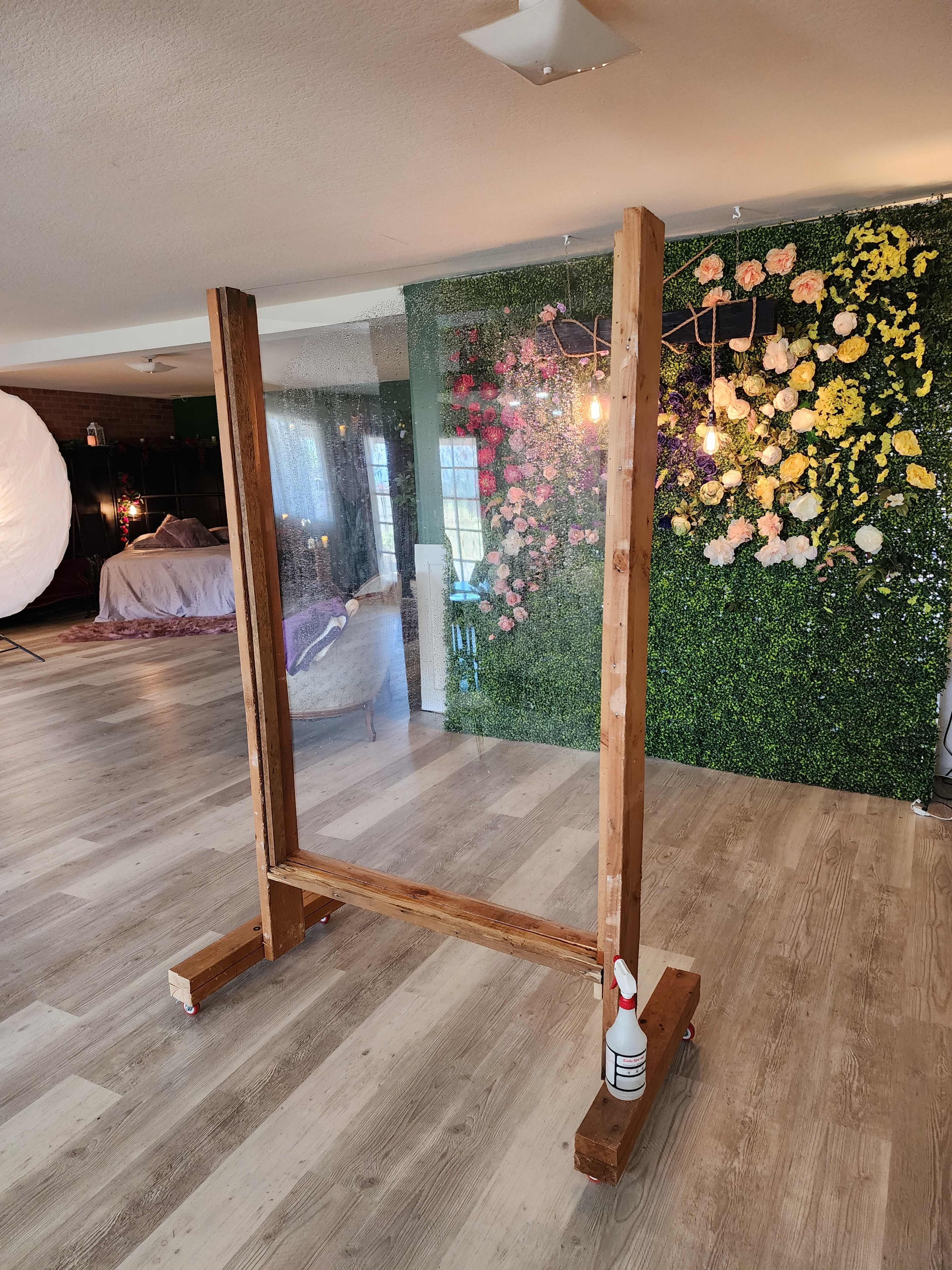 The image features a wooden frame with a clear partition located in a room with a floral accent wall and a bed in the background.