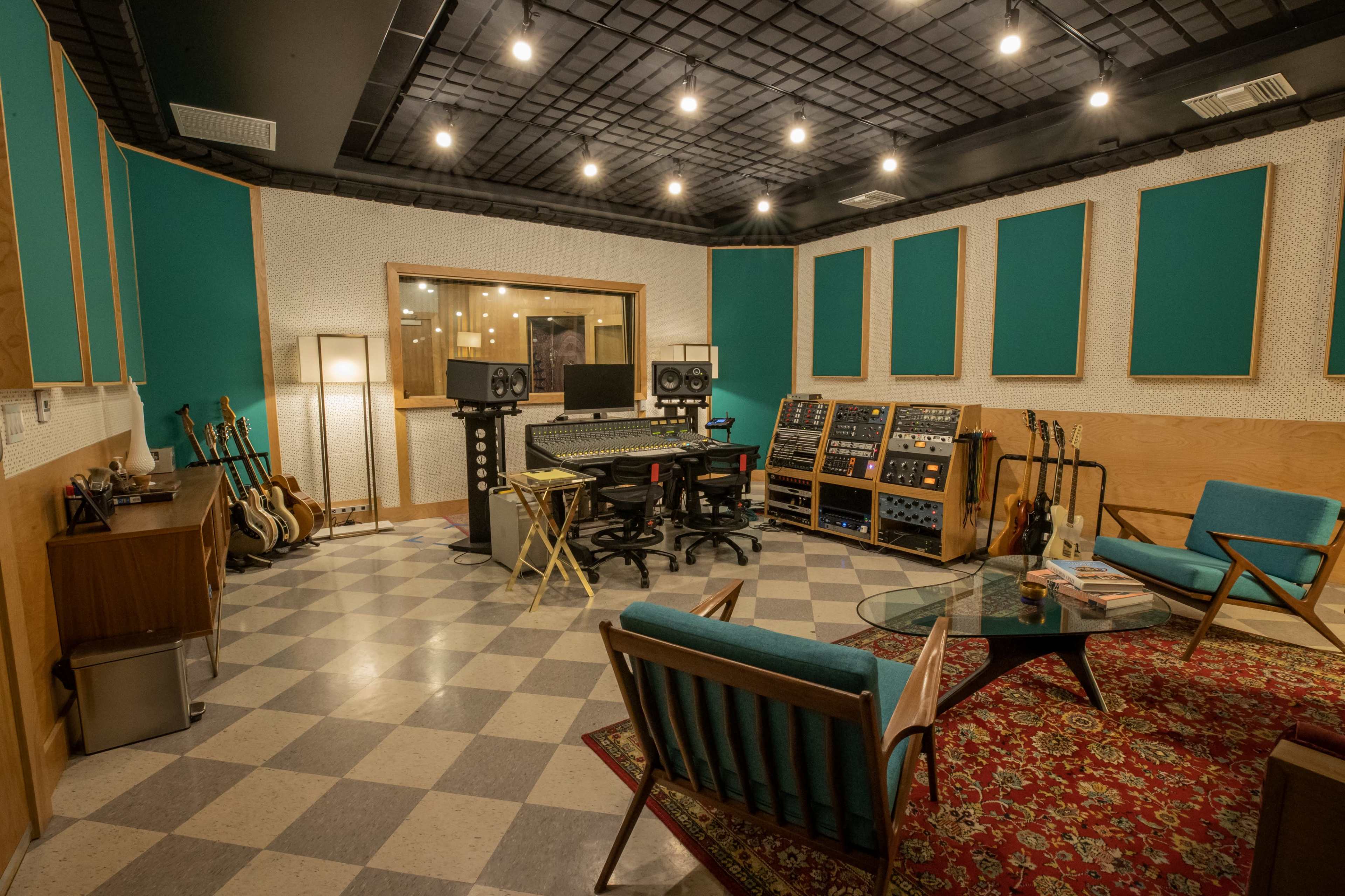 A recording studio with a control desk, multiple guitars, and a patterned carpet.