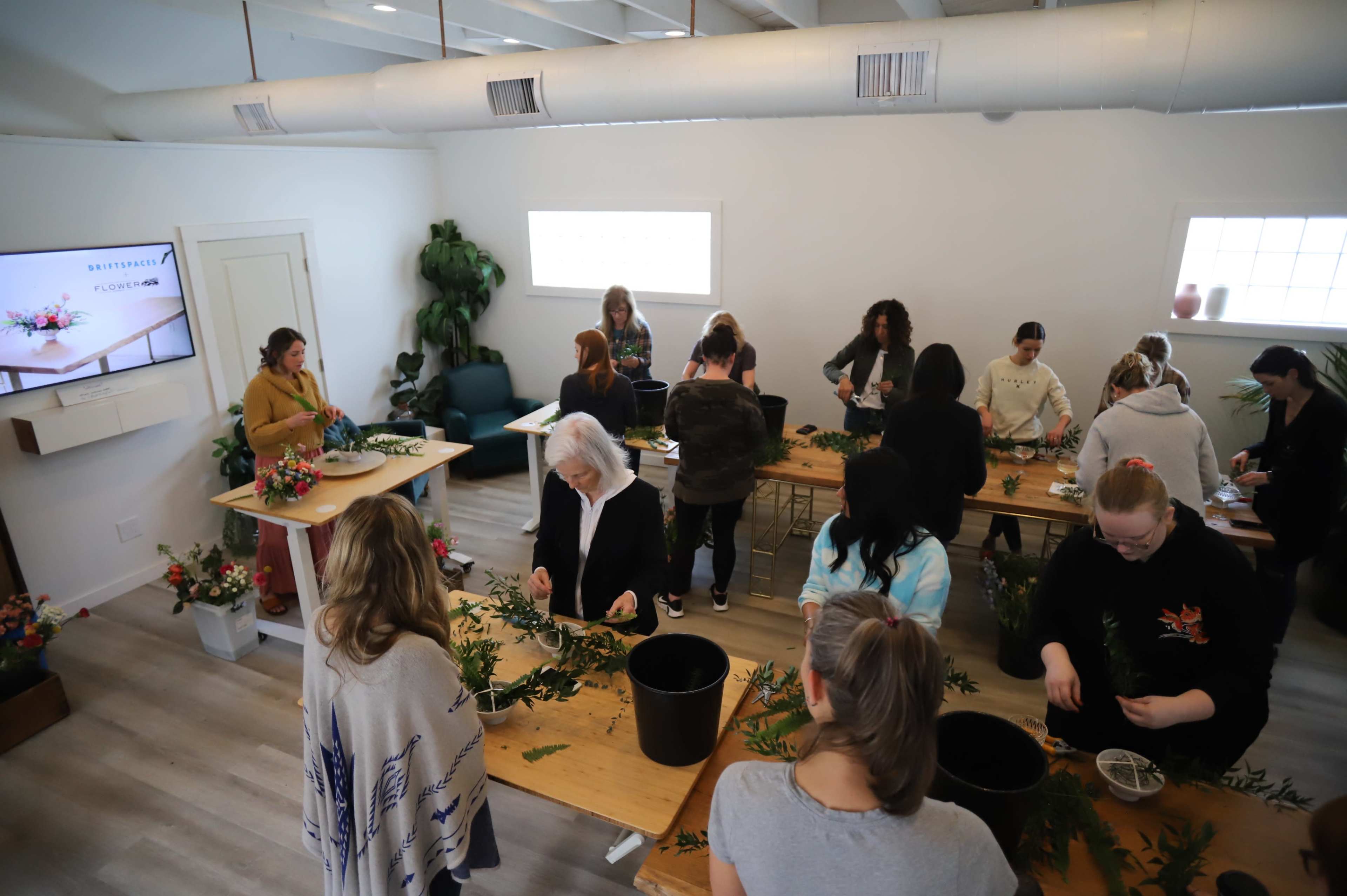 A group of people participate in a floral arrangement workshop inside a well-lit, modern studio space.