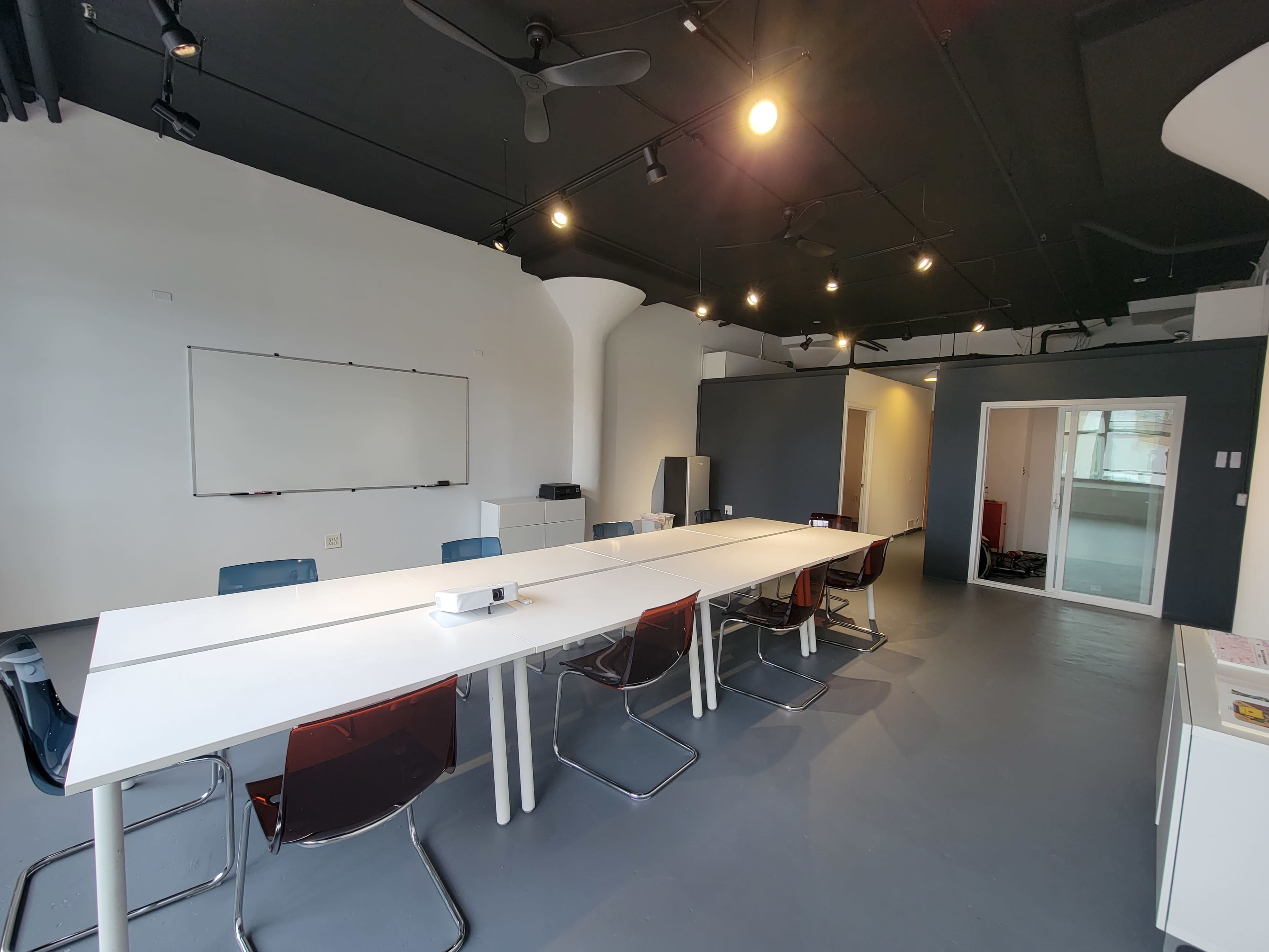 A modern conference room with a long white table, transparent chairs, and a whiteboard on the wall.