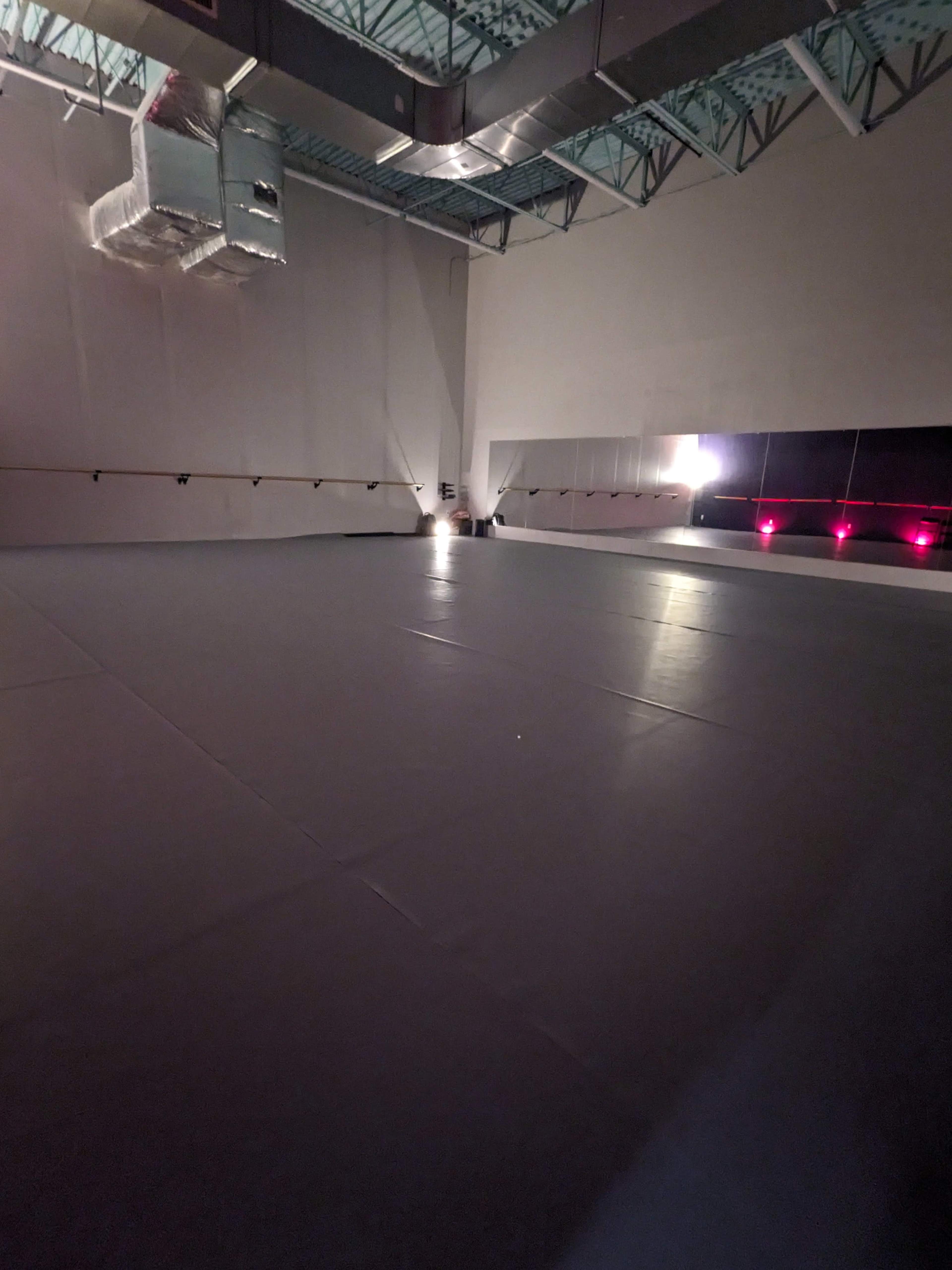The image shows an empty indoor studio with gray mats on the floor and soft lighting.