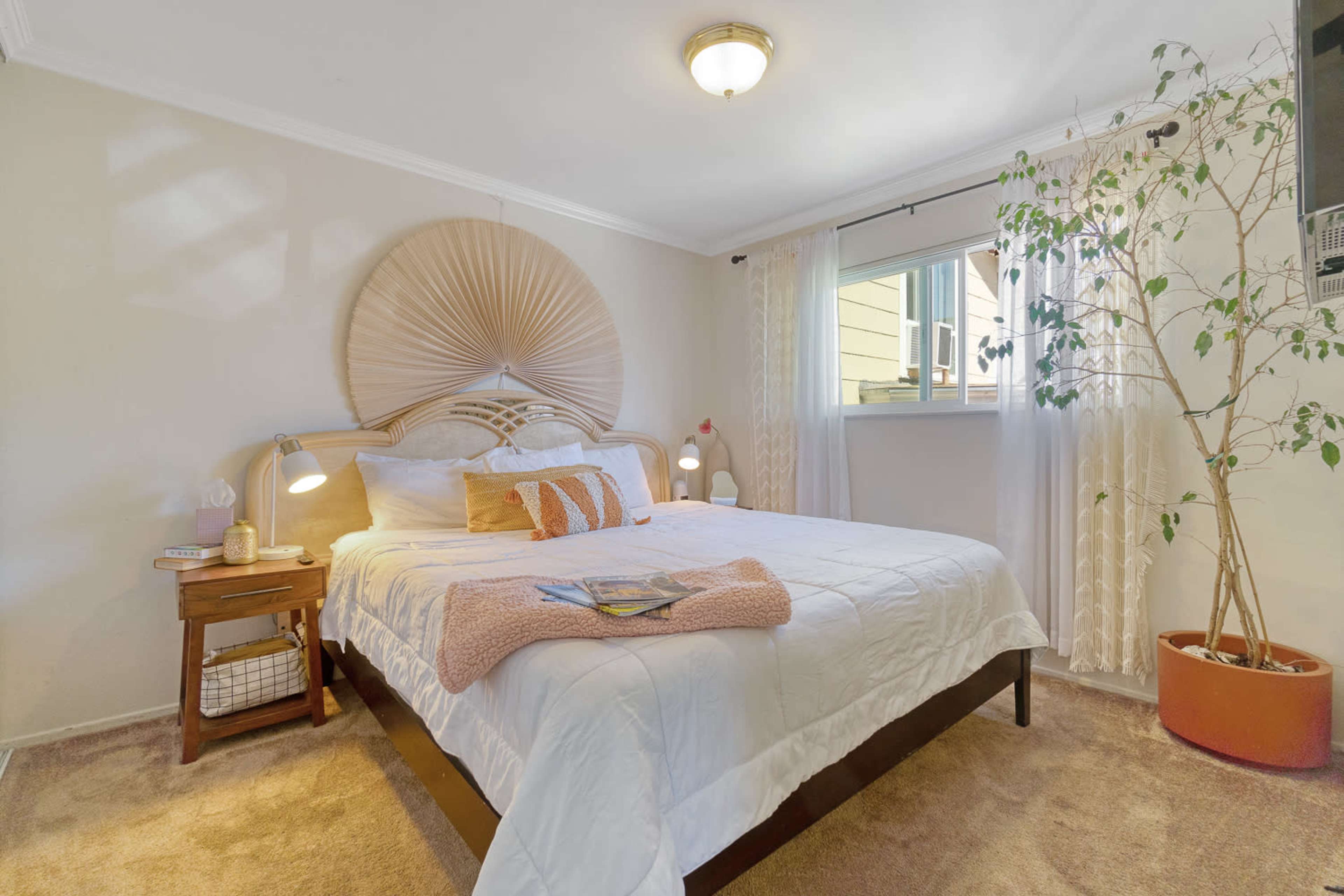 A well-appointed bedroom featuring a bed with a decorative headboard, bedside tables with lamps, and a plant near a window.