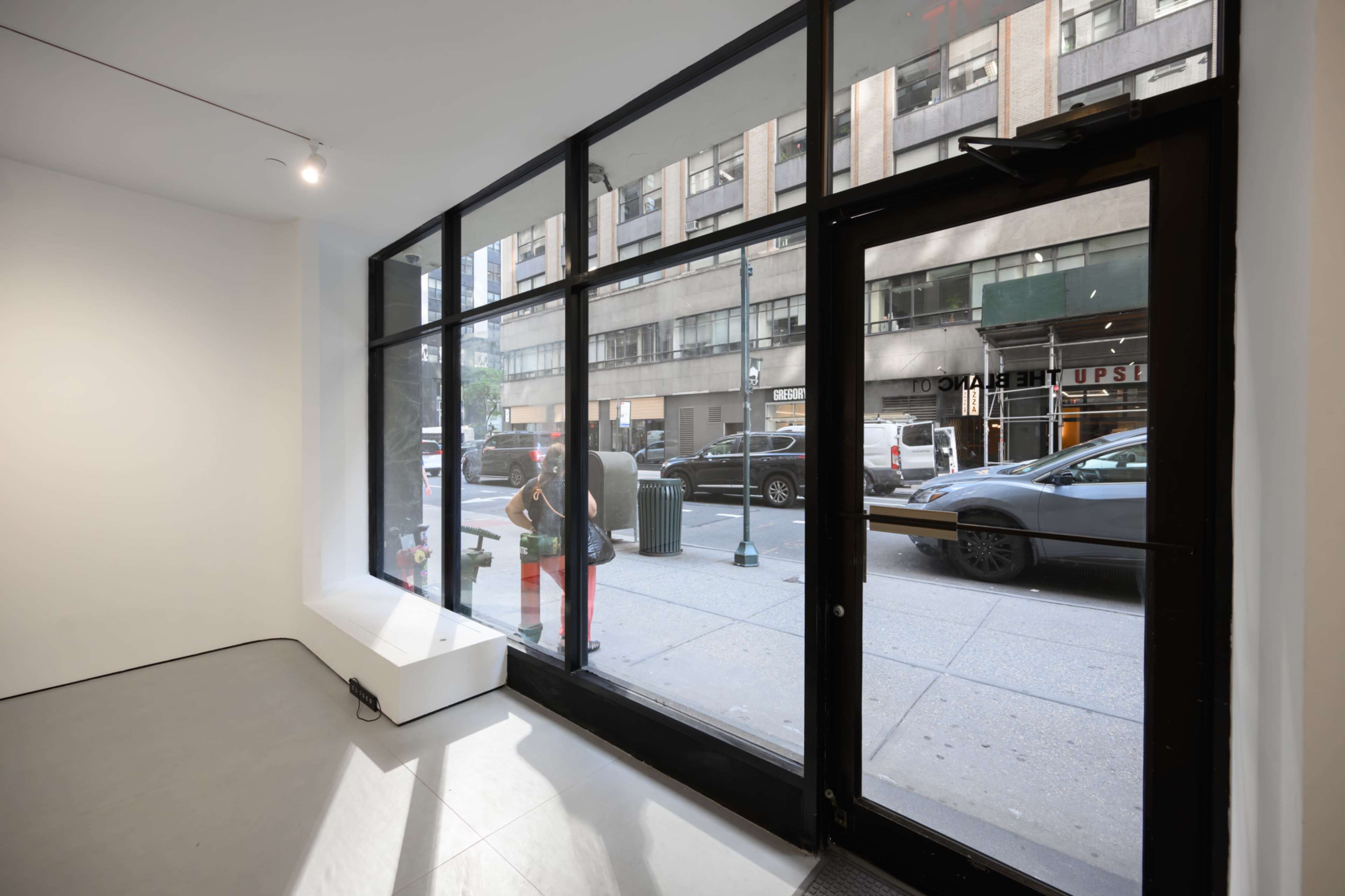 The image shows the interior of a storefront with large glass windows facing a busy street where cars are parked and passing by.