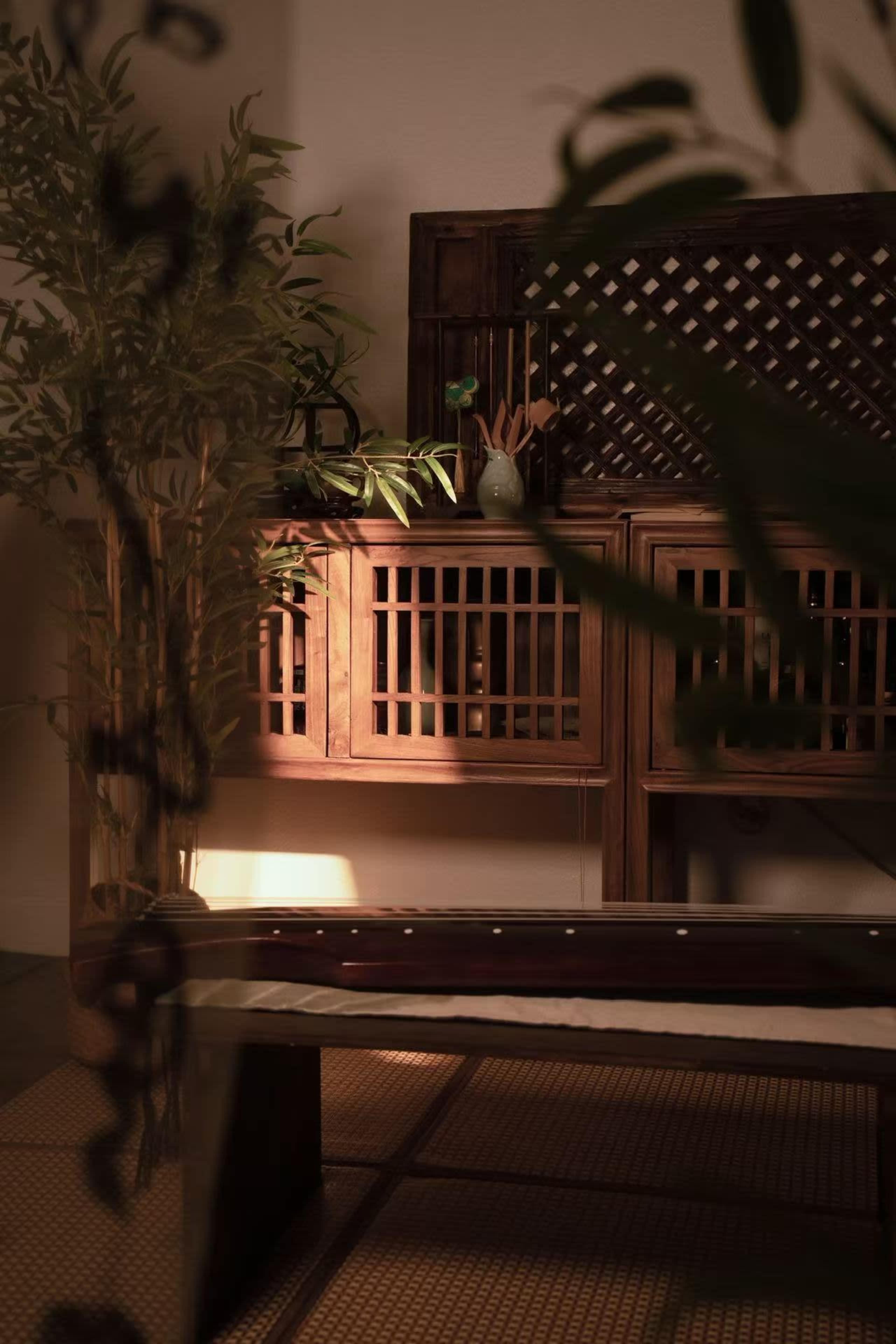 The image depicts a tranquil indoor space with wooden furniture, a bamboo plant, and soft lighting highlighting traditional elements.