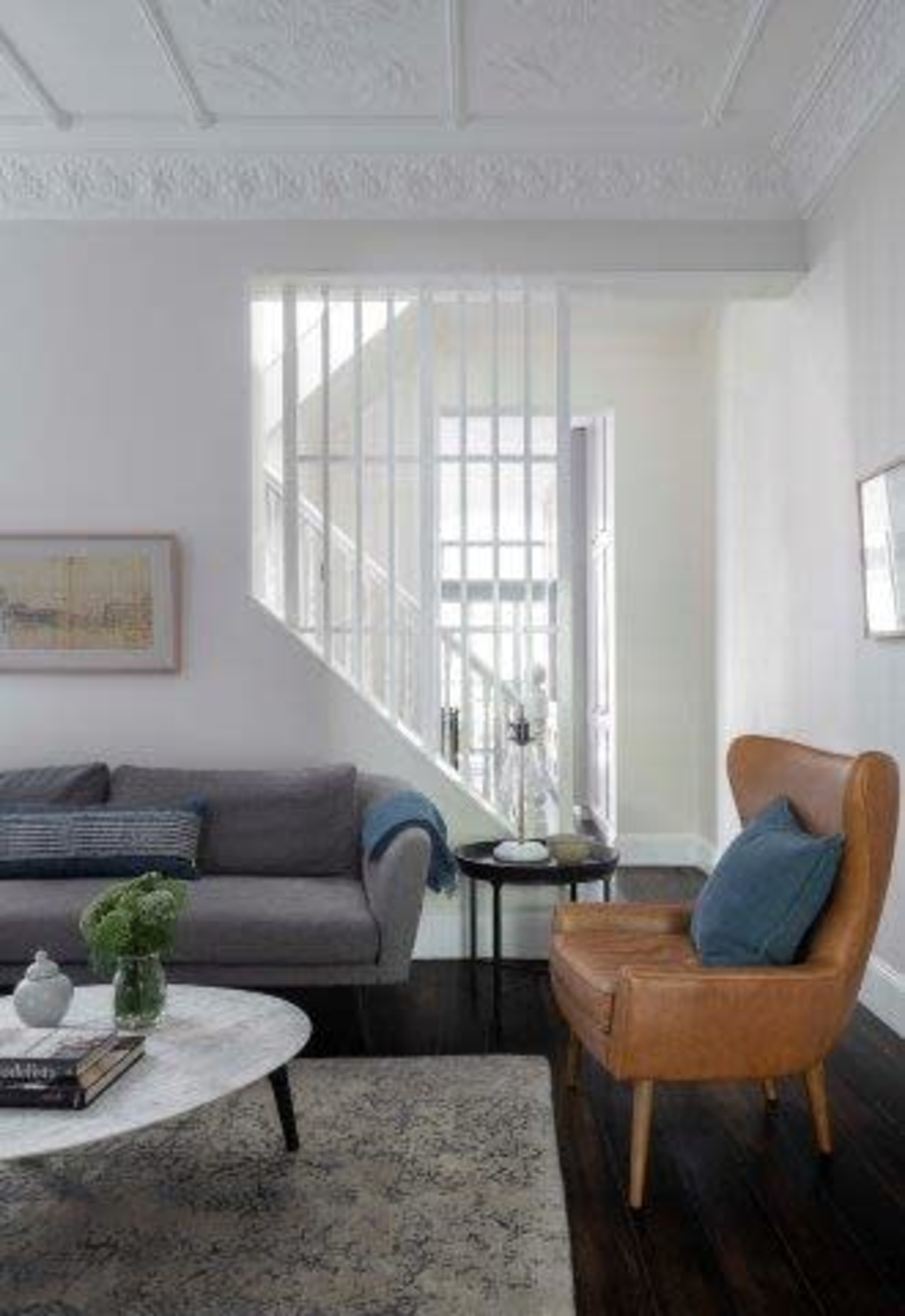 A modern living room features a gray sofa, a brown armchair, a marble coffee table, and a staircase in the background.