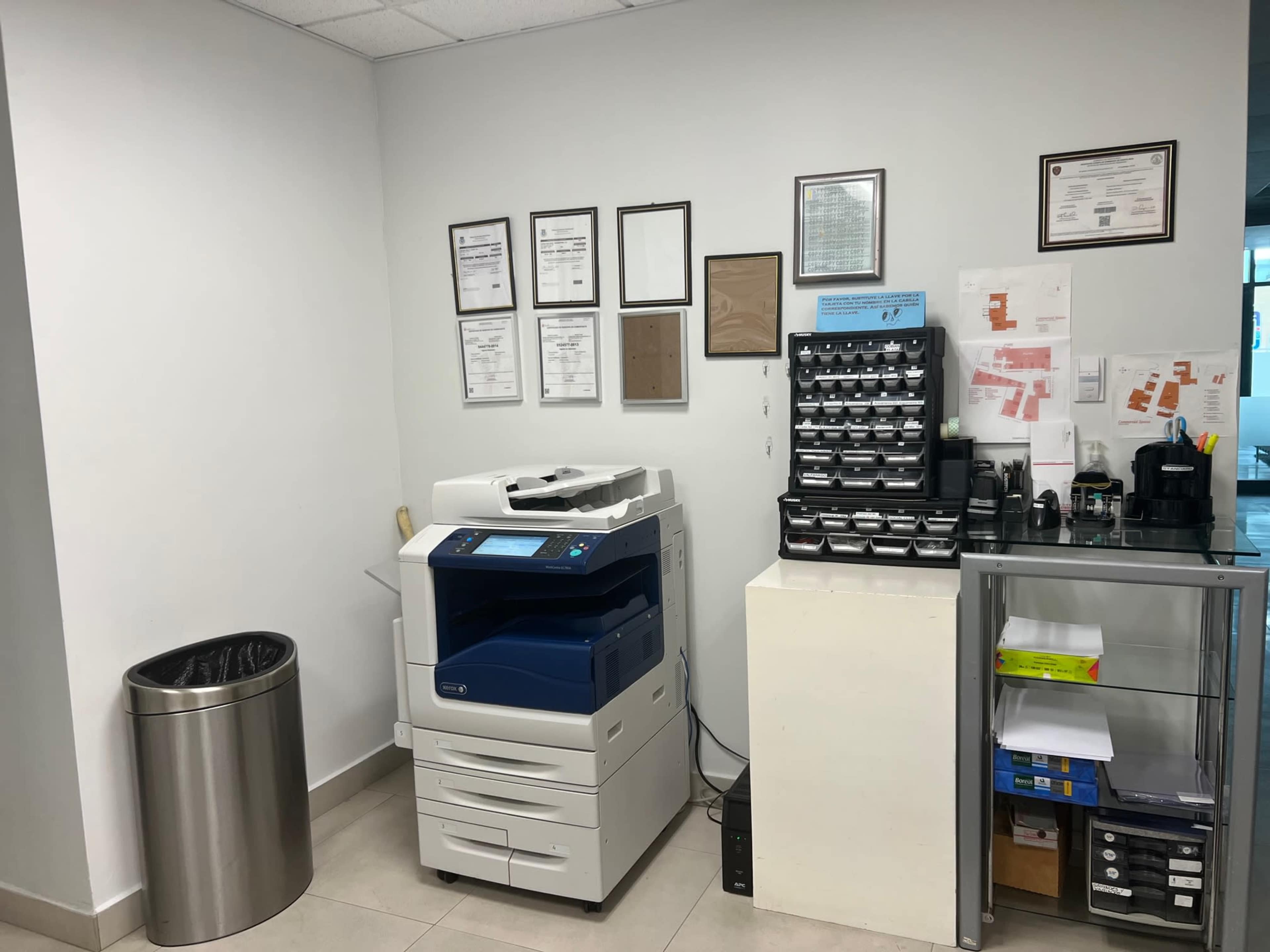 The image shows an office corner with a multi-function printer, a trash can, and a shelf filled with organized office supplies and documents on the wall.