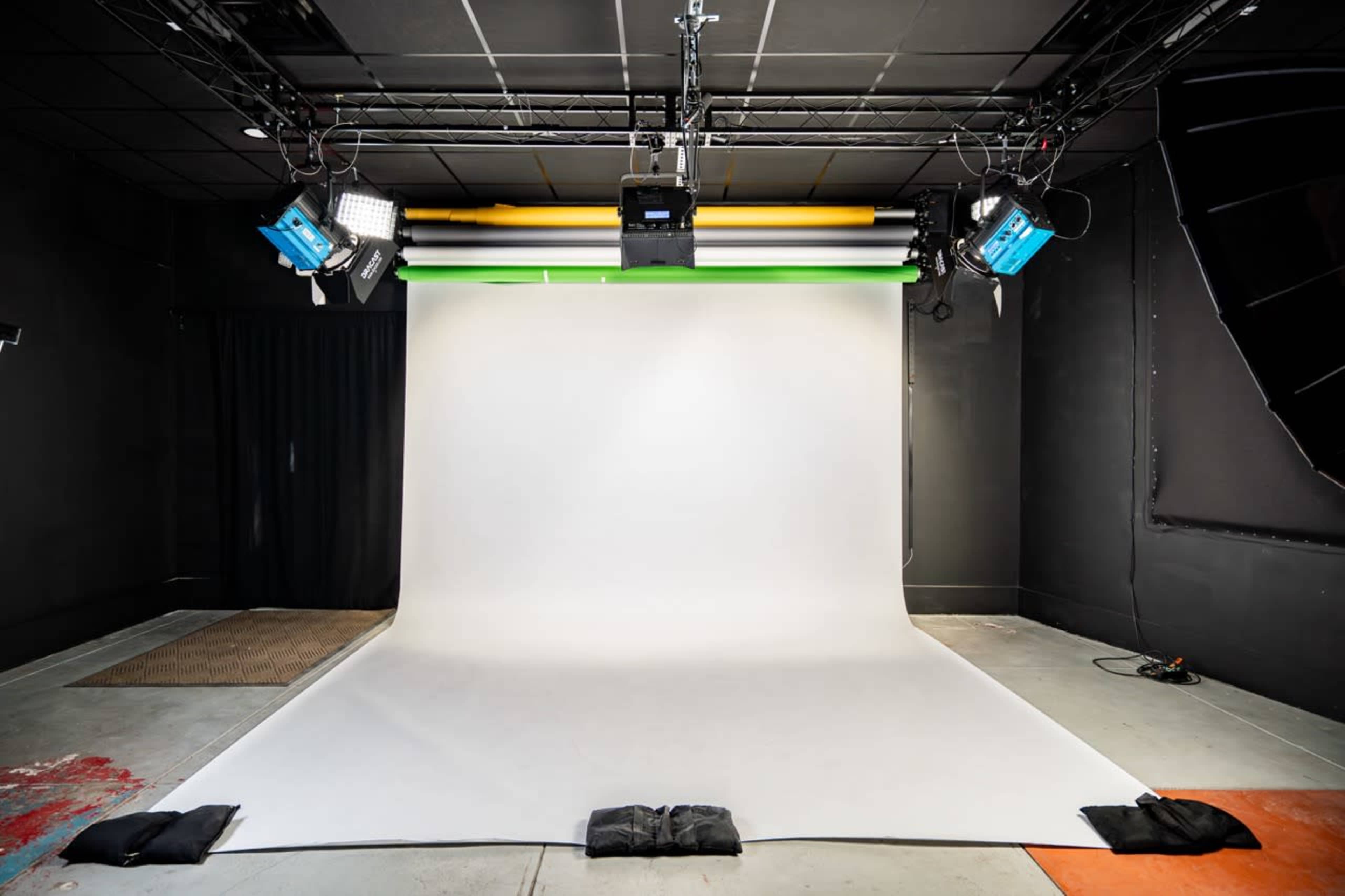 The image shows a photography studio with a white backdrop, professional lighting setups, and a black curtain on one side.