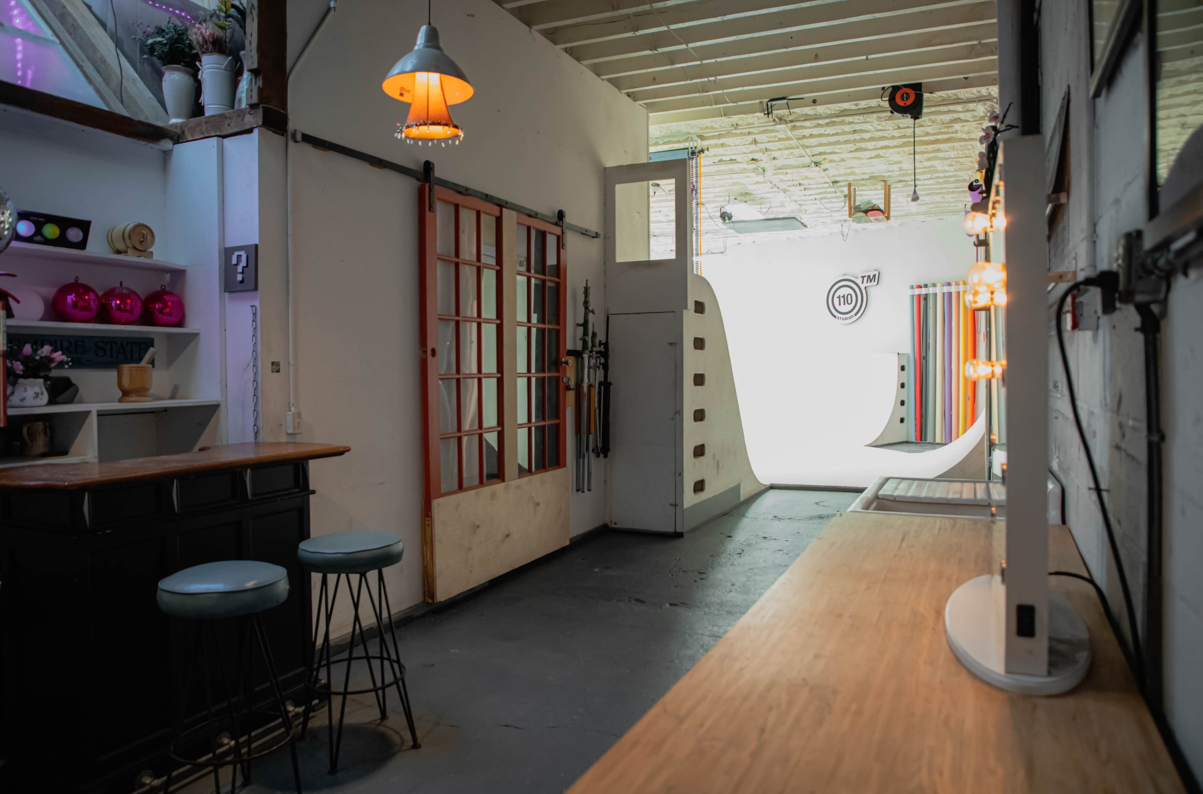 The image shows an indoor space featuring a bar with stools, a red-framed door, and a brightly lit area with colorful backgrounds at the end of the hallway.
