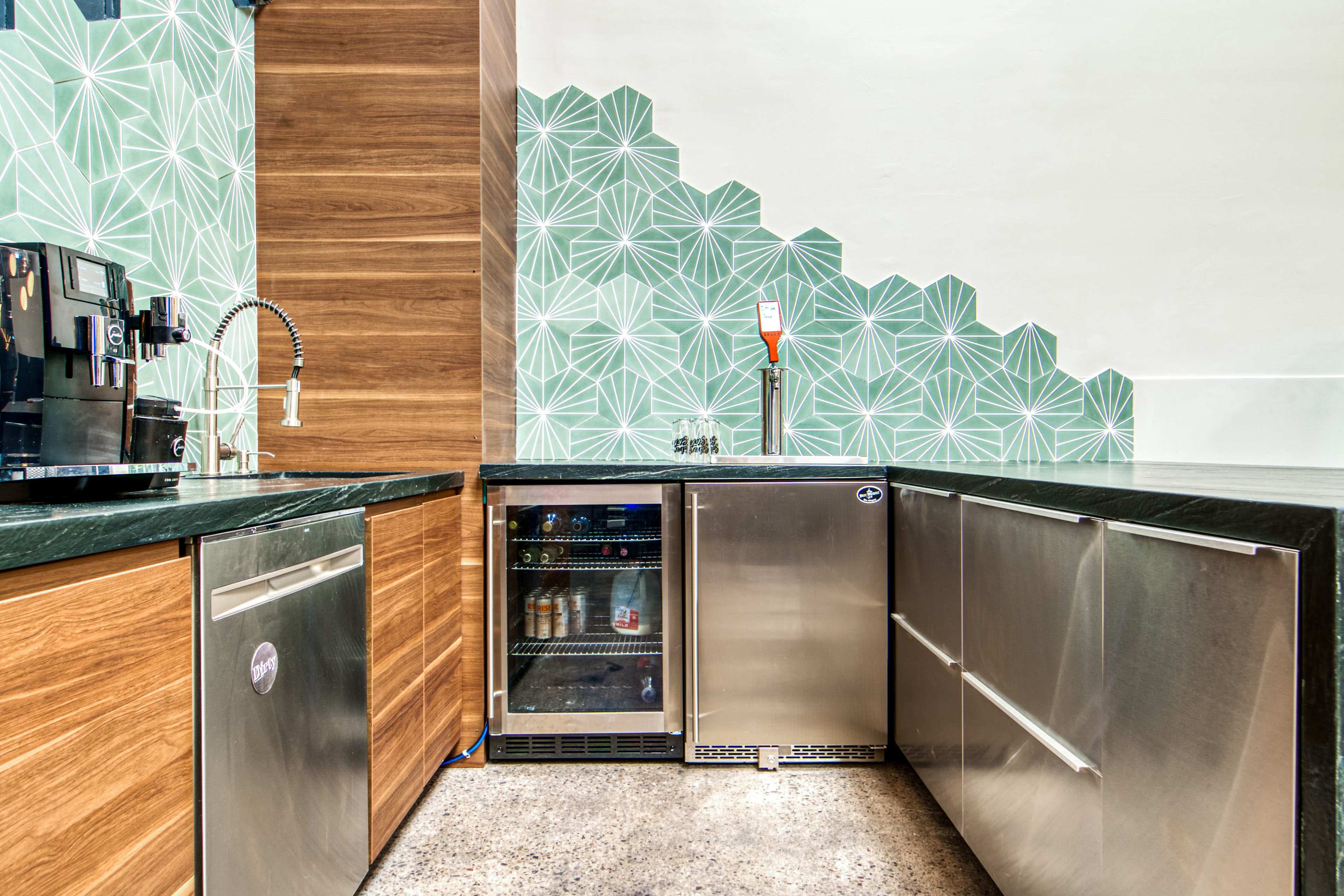 A modern kitchen with wooden cabinets, stainless steel appliances, and a geometric patterned wall.