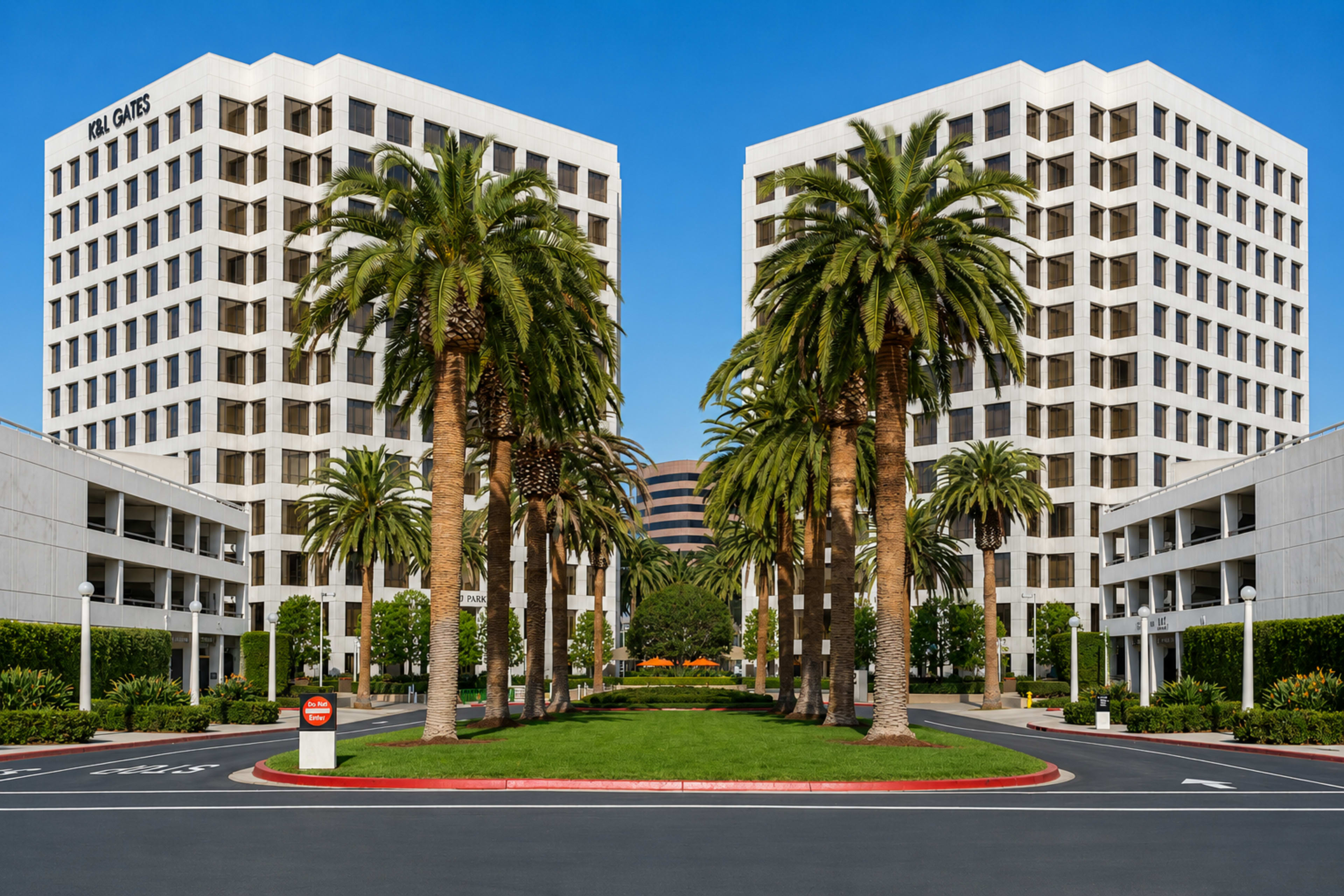 The image shows two modern office buildings flanked by palm trees and landscaped greenery, with a clear blue sky overhead.