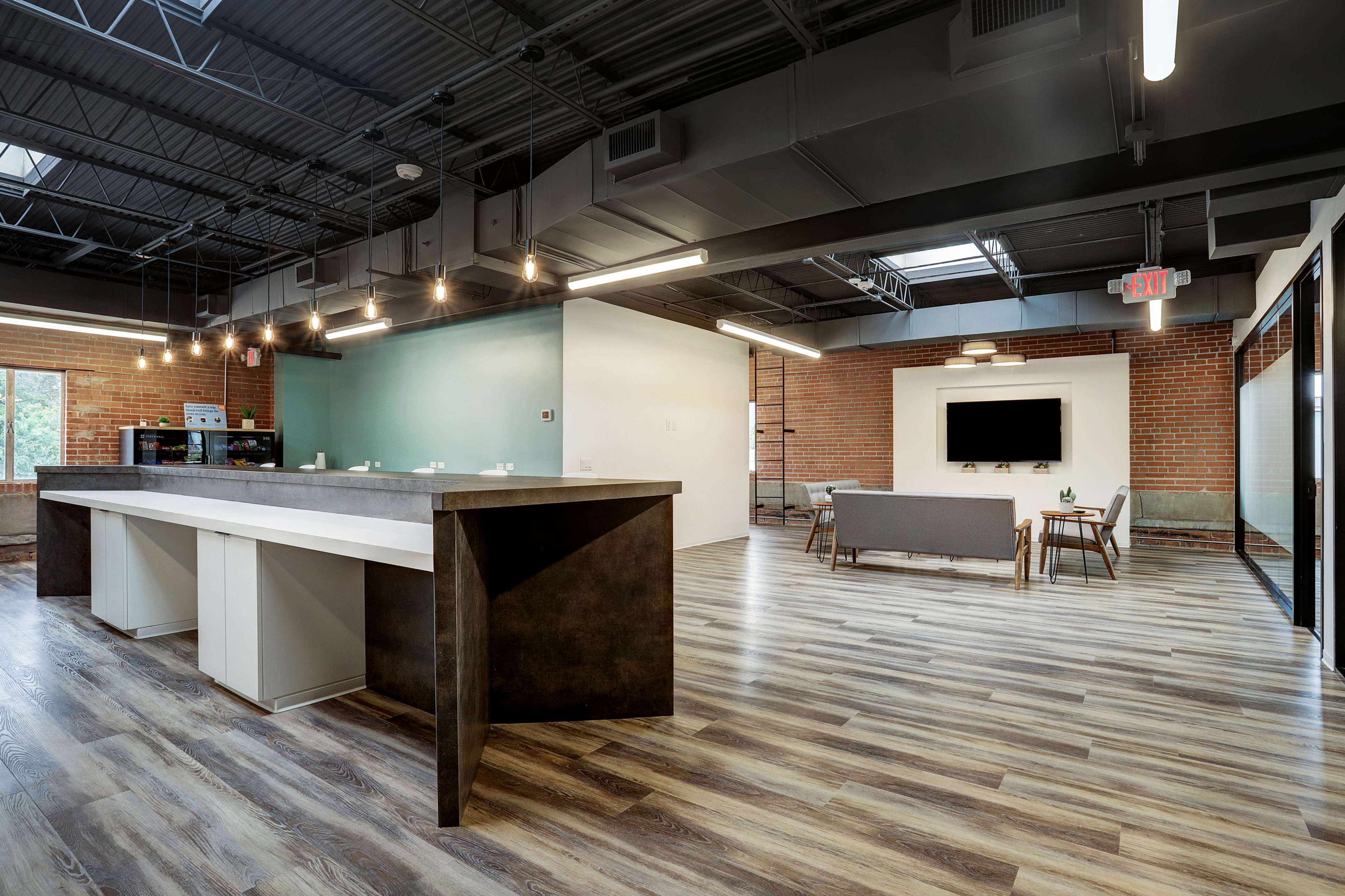 A modern office space with a large kitchen island, wooden flooring, and a seating area featuring a couch and a television on the wall.